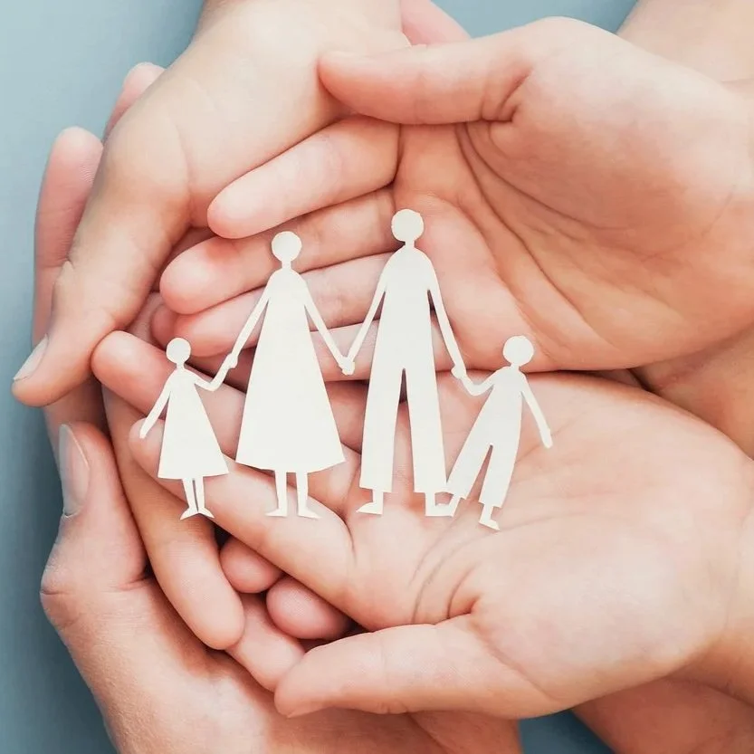 A paper cutout of a family holding hands is placed inside two adult hands.