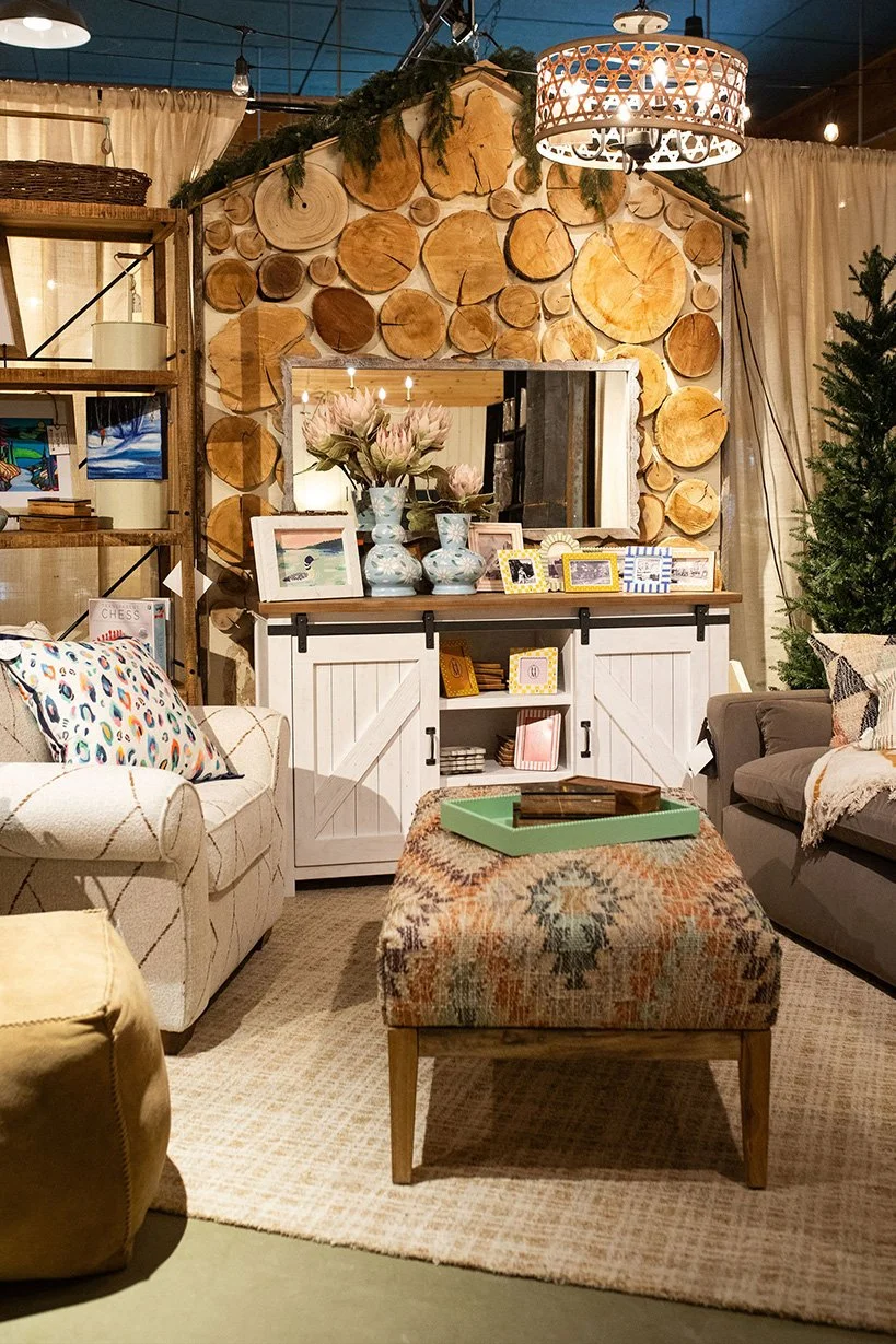 Living room with a wood log wall feature, a mirror, books, framed photos, a floral arrangement, and a seating area including a sofa, an ottoman, and a rug.