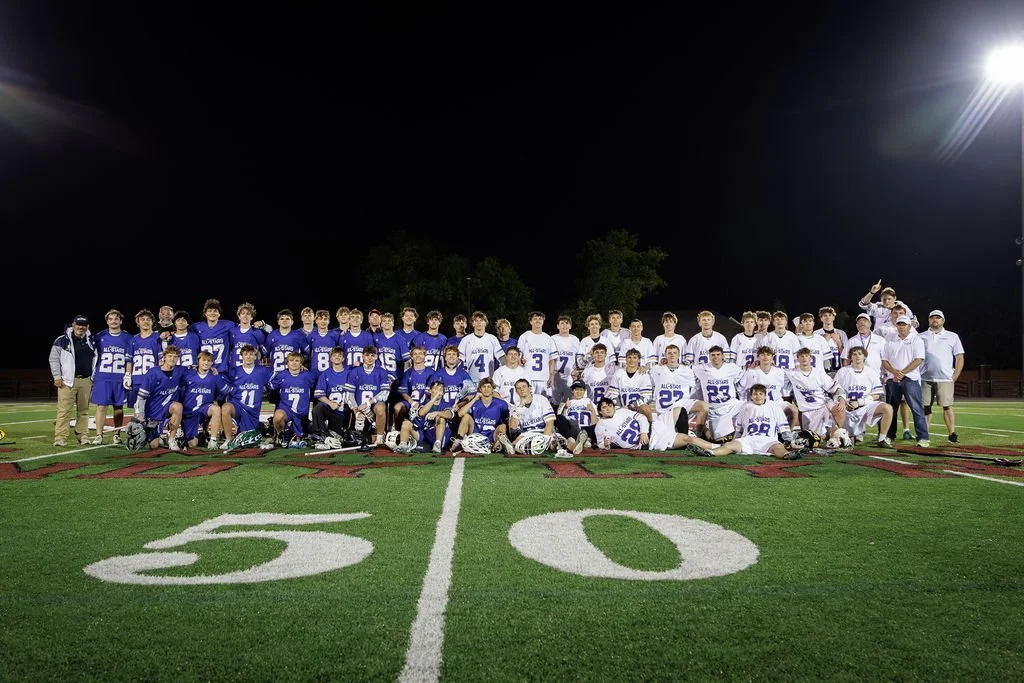 Group of high school football players and coaches on a football field at night for a team photo.