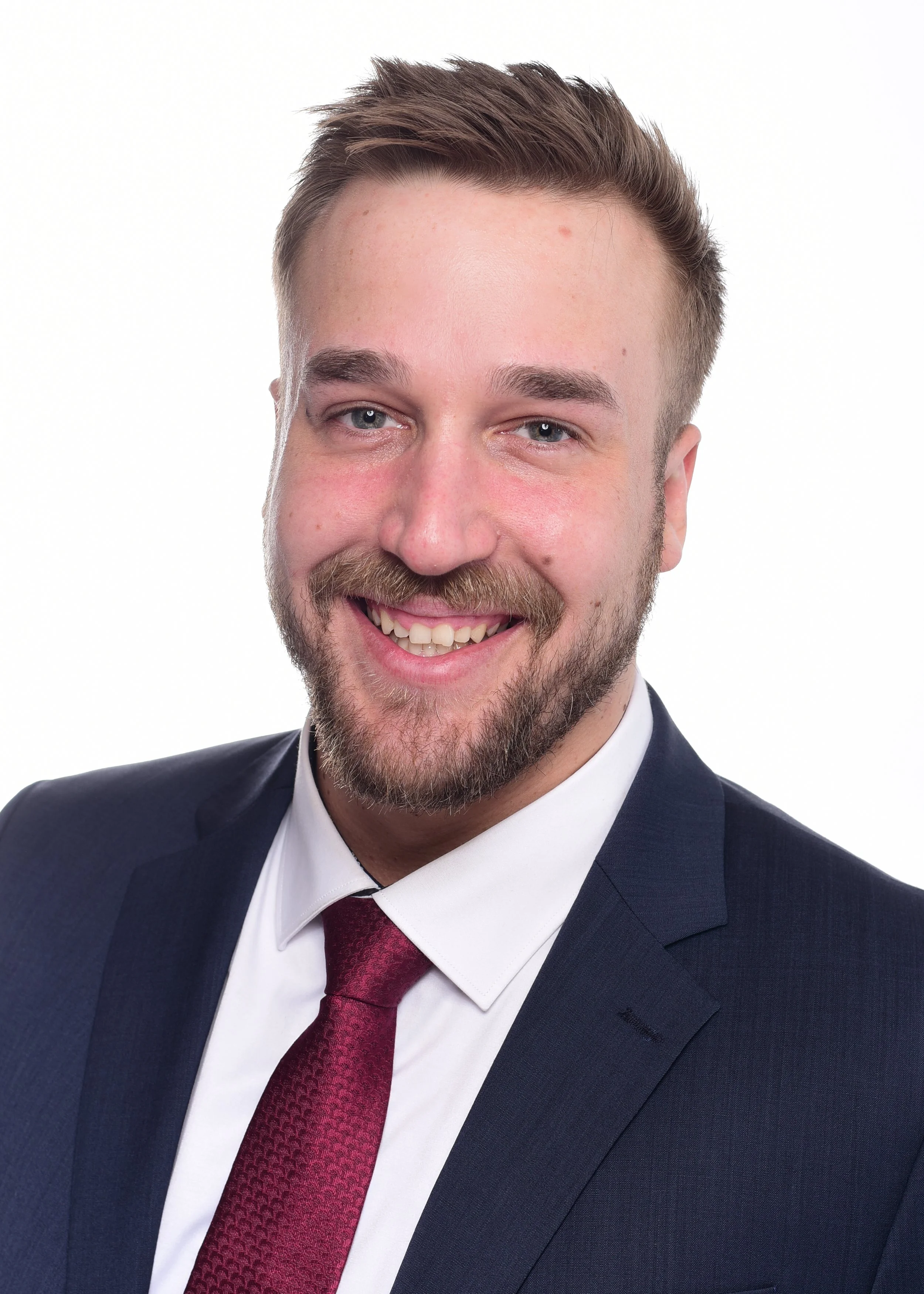 Porträt eines lachenden Mannes in formeller Kleidung vor weißem Hintergrund.