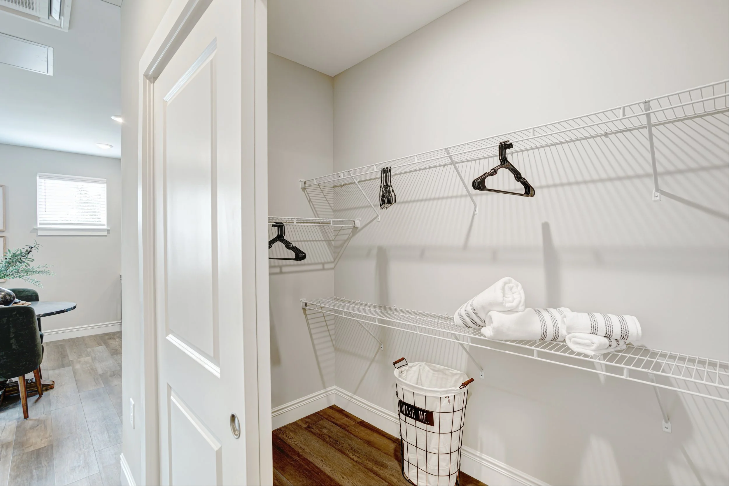 Empty white wire shelf in a laundry closet with folded towels and laundry basket below.
