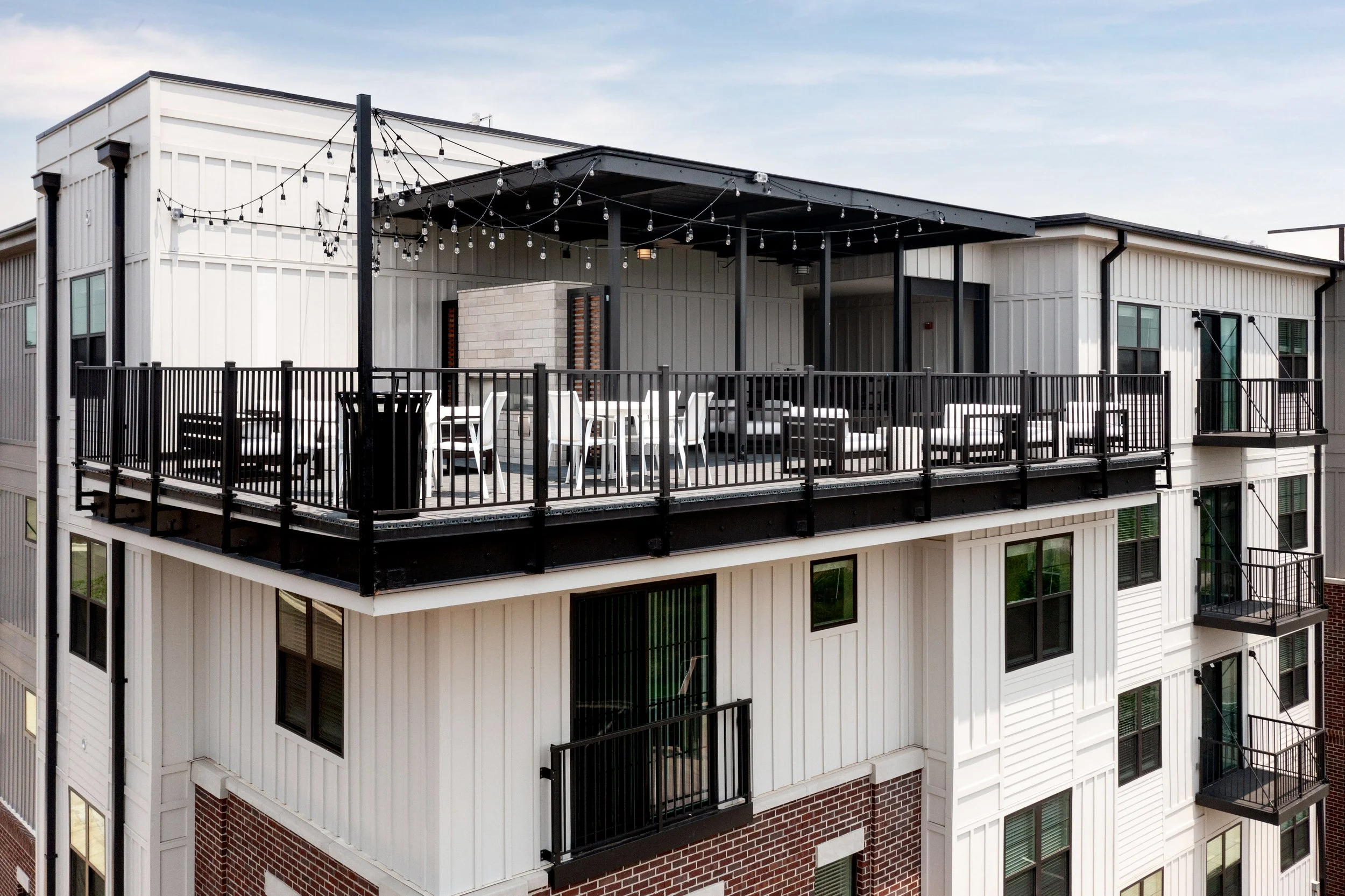 A rooftop terrace on a high-rise building with string lights, outdoor furniture, and a view of the sky.