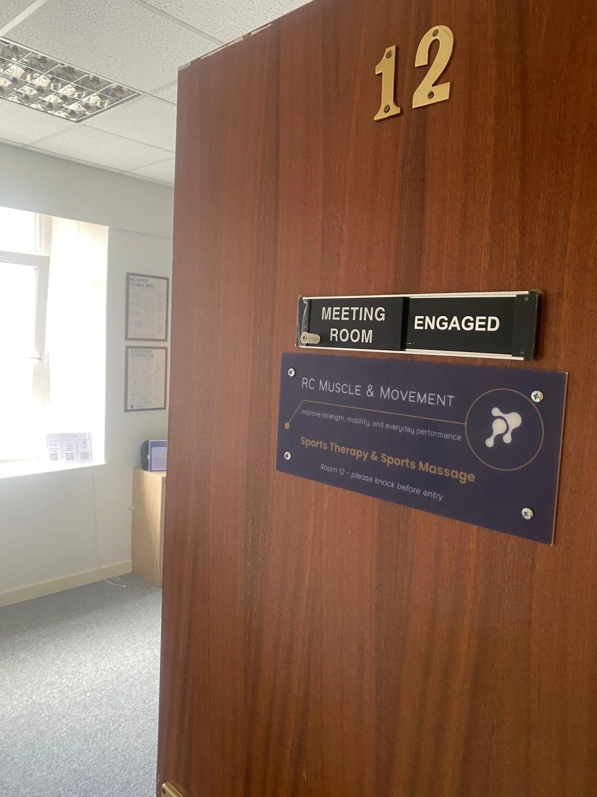 an open door going into a clinic with a sign that says RC Muscle & Movement , sports therapy and sports massage , room 12 please knock before entry