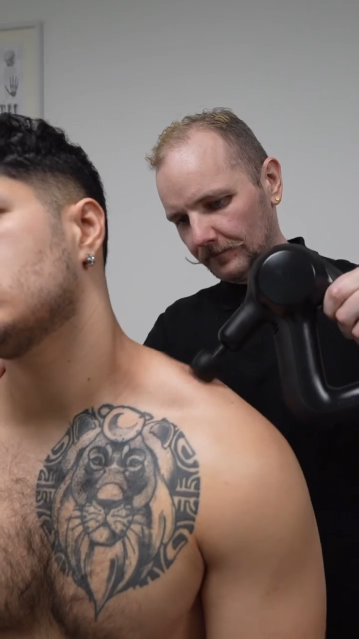 sports therapist using percussion gun on shoulders during massage therapy