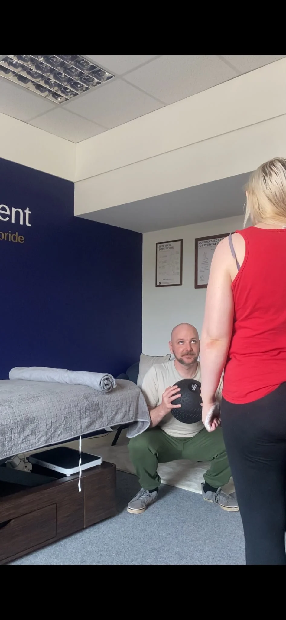 sport therapist demonstrating weighted squat to another adult in clinic