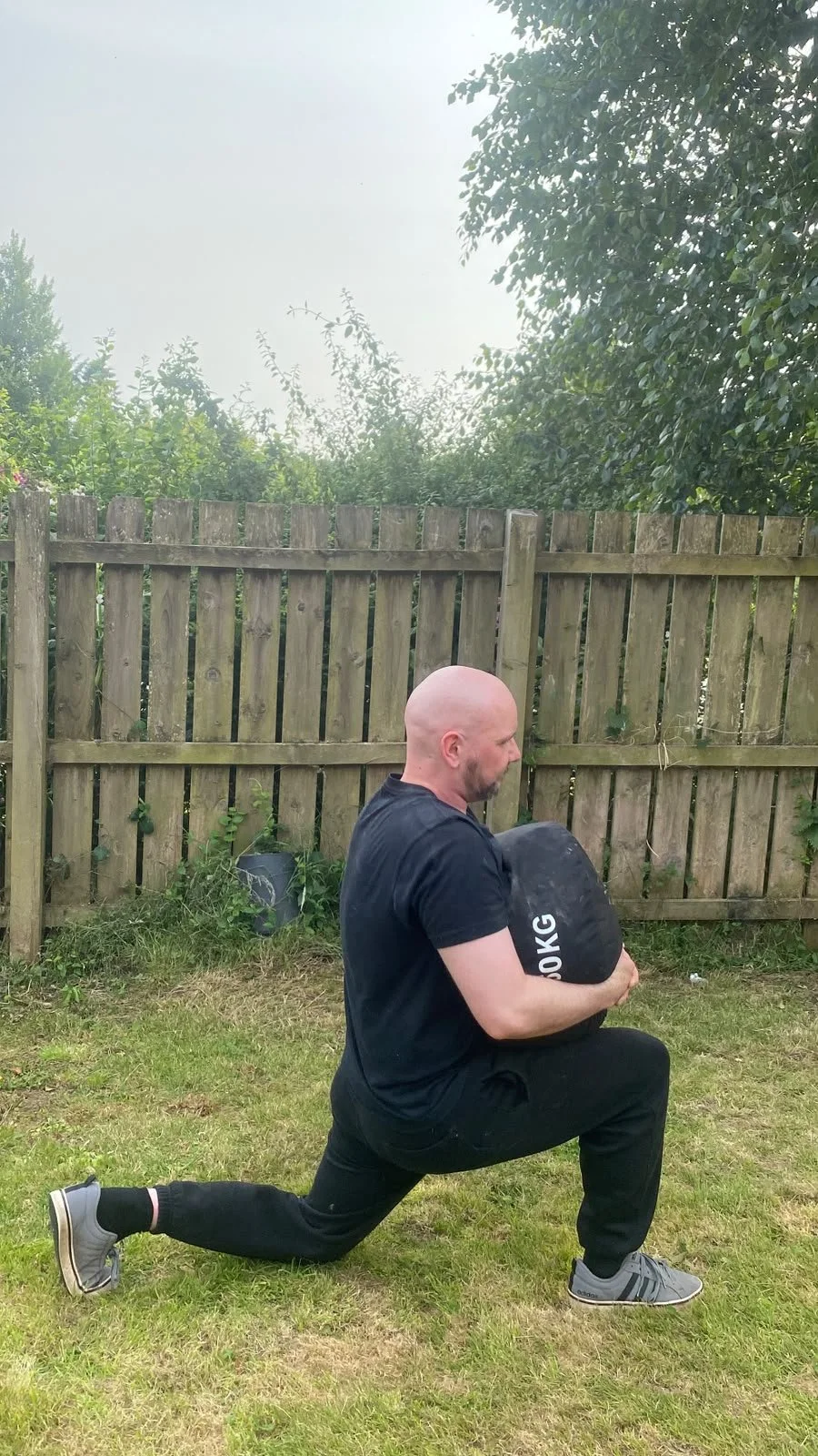 sport therapist Ross demonstrating a lunge with a weighted sandbag showing how weight changes an exercise