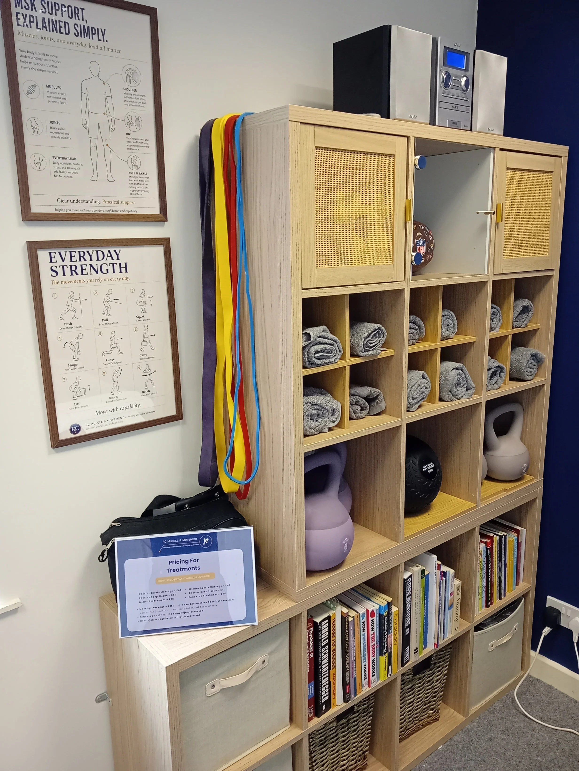educational frame pictures on msk support , everyday strength and shelving unit showing books , towels , exercise rehab equipment in rc muscle and movement sports therapy clinic situated in east kilbride