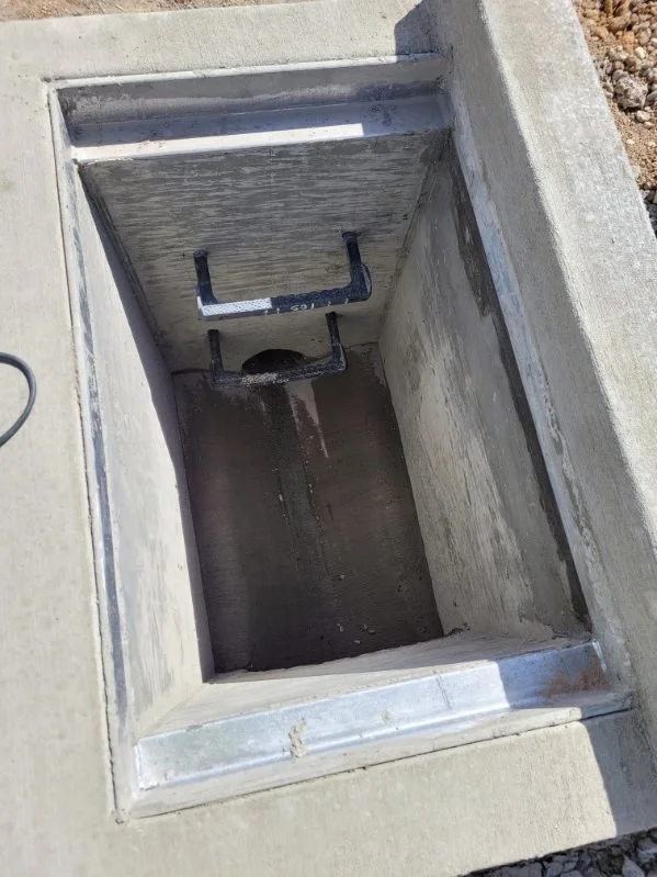 Empty concrete storm drain with metal guard at the bottom, located on a sidewalk.
