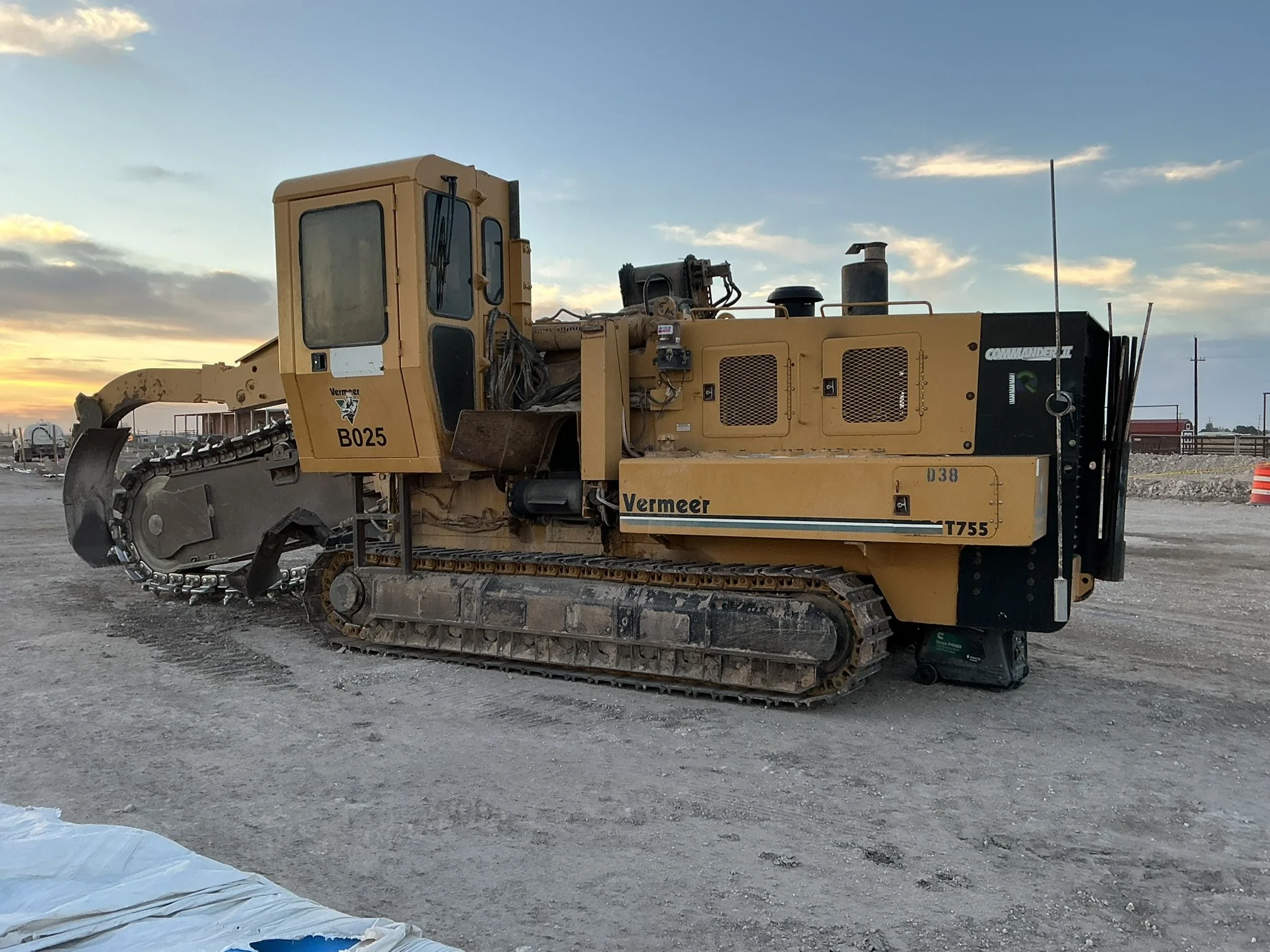 A large yellow Vermeer T755 tracked excavator with a cutter head attachment on a construction site at sunset.
