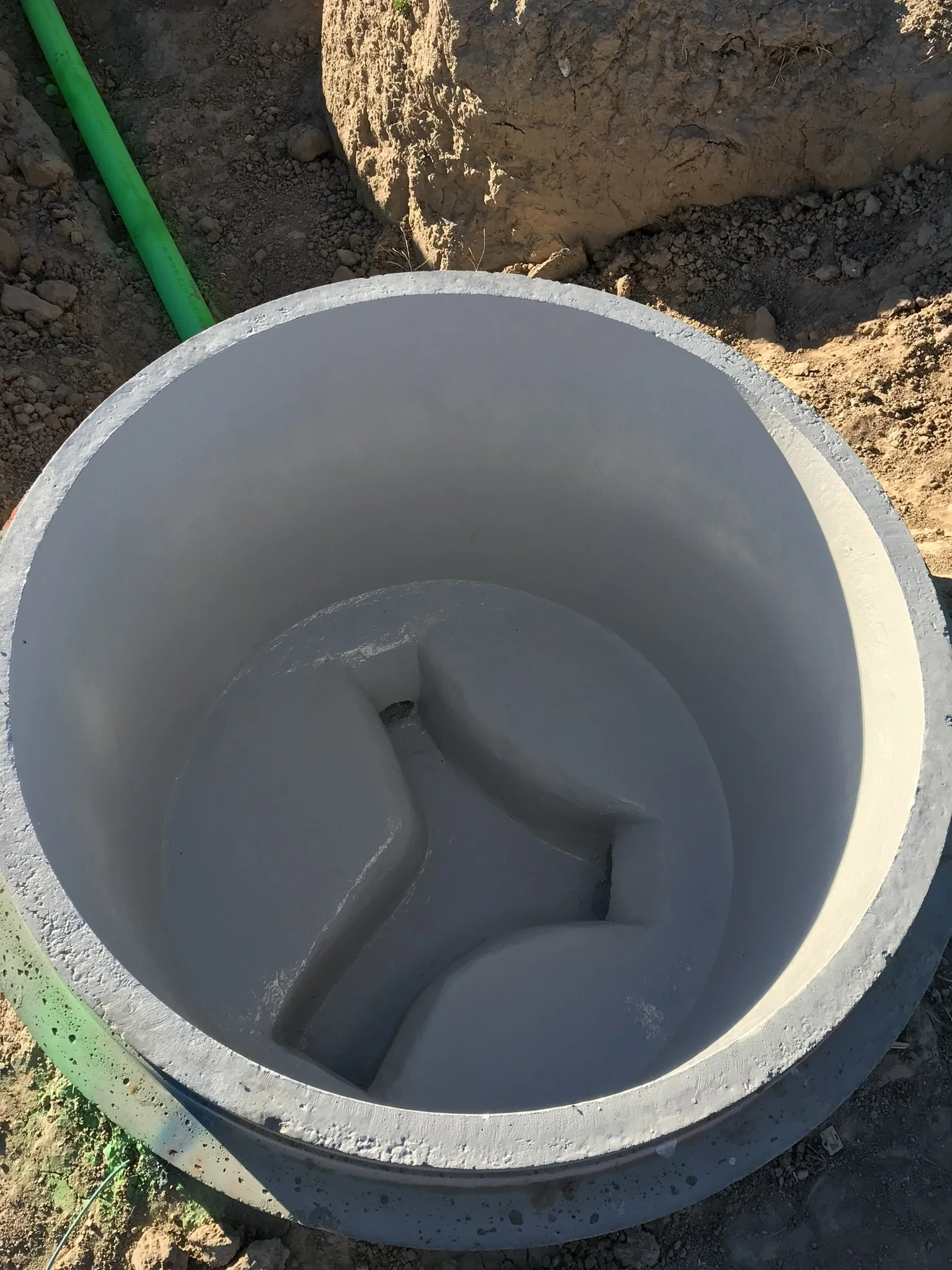A large, round concrete structure with internal stairs, possibly a sump or septic tank, installed in a dirt area with a green pipe nearby.