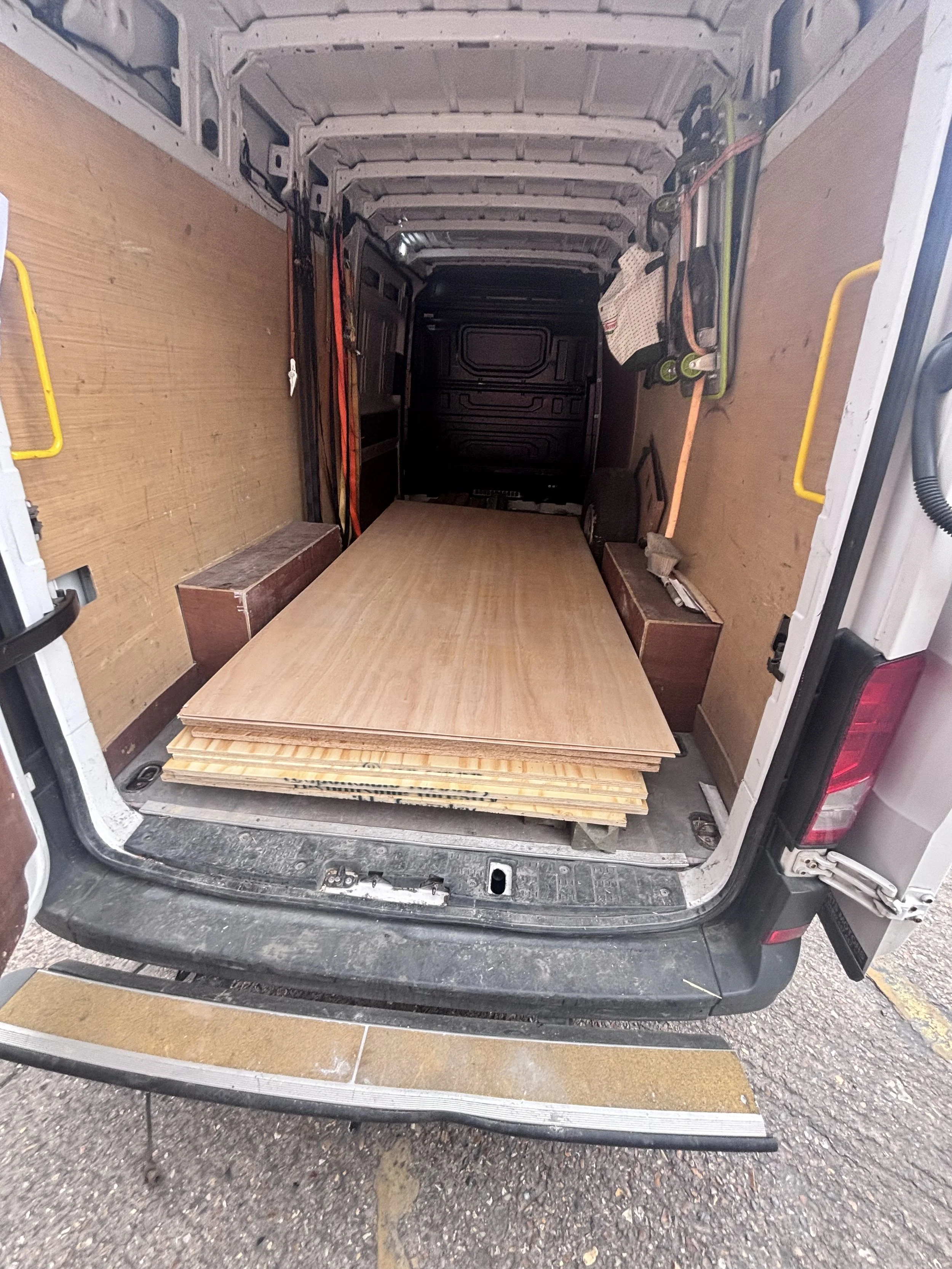 View of the empty cargo area of a van with some wooden boards and tools stored inside.