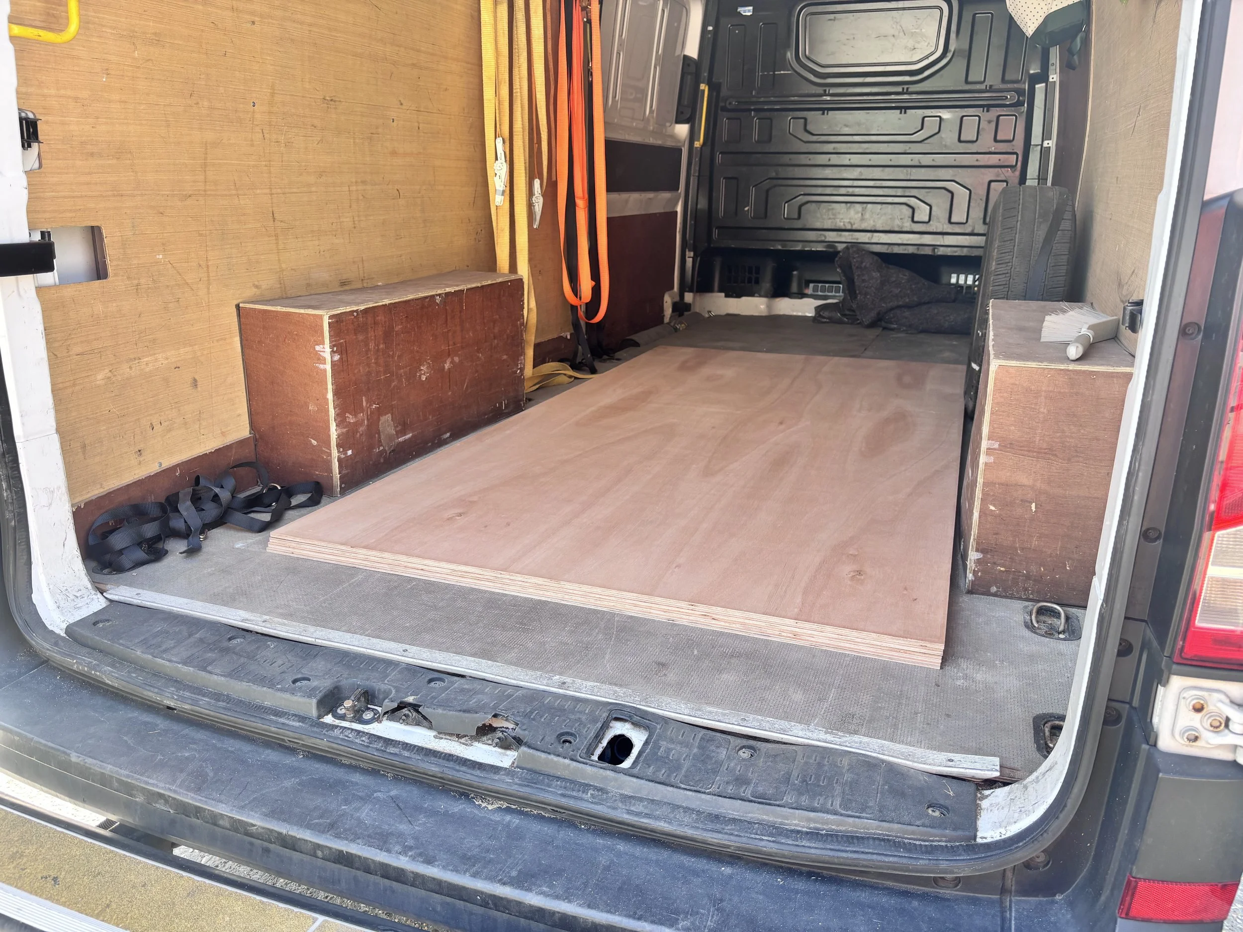 Open van trunk showing a wooden interior with some tools, straps, and a small wooden box stored inside.