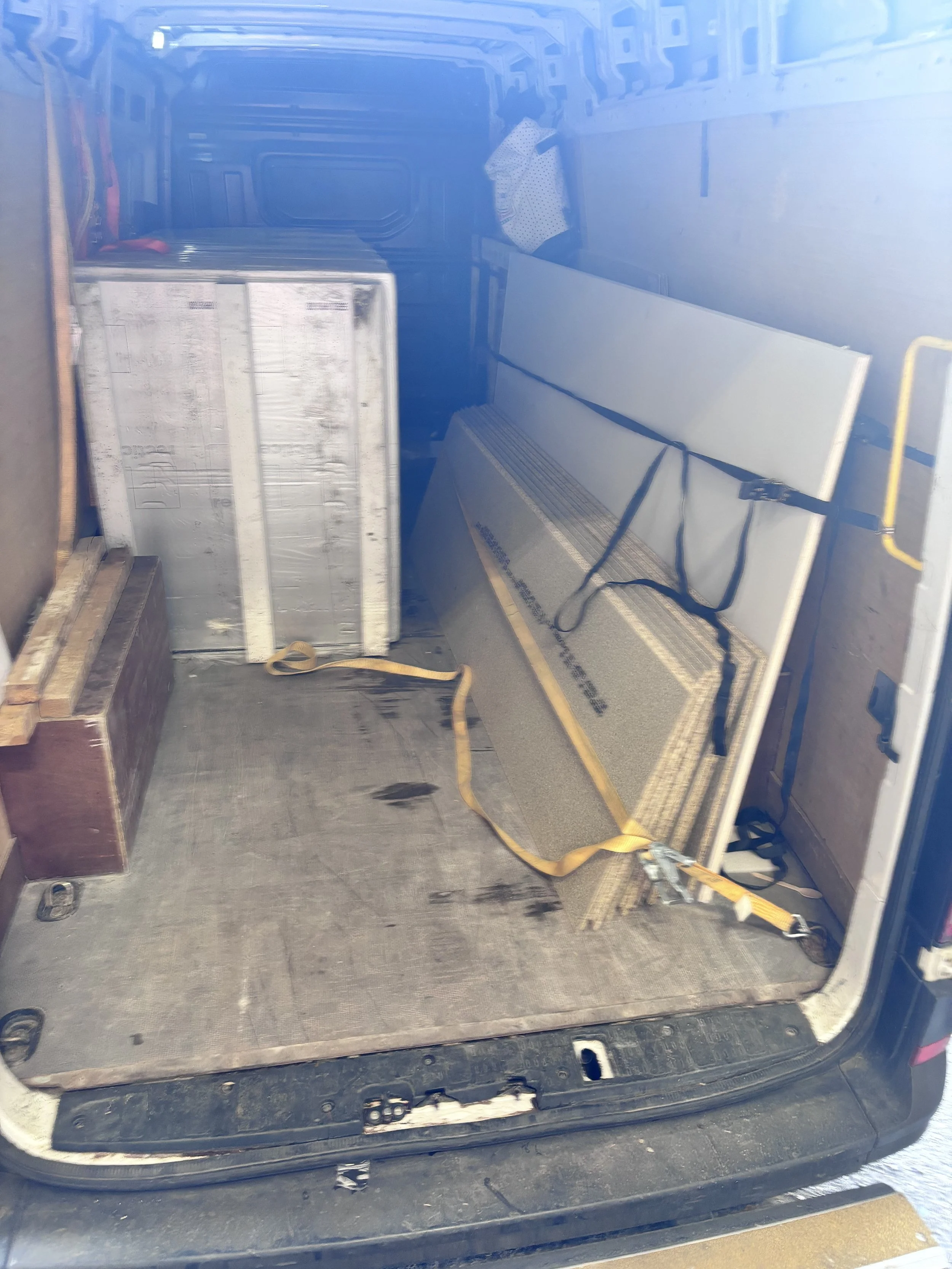 Empty vehicle trunk with a large metal box, a piece of carpet, and straps inside.