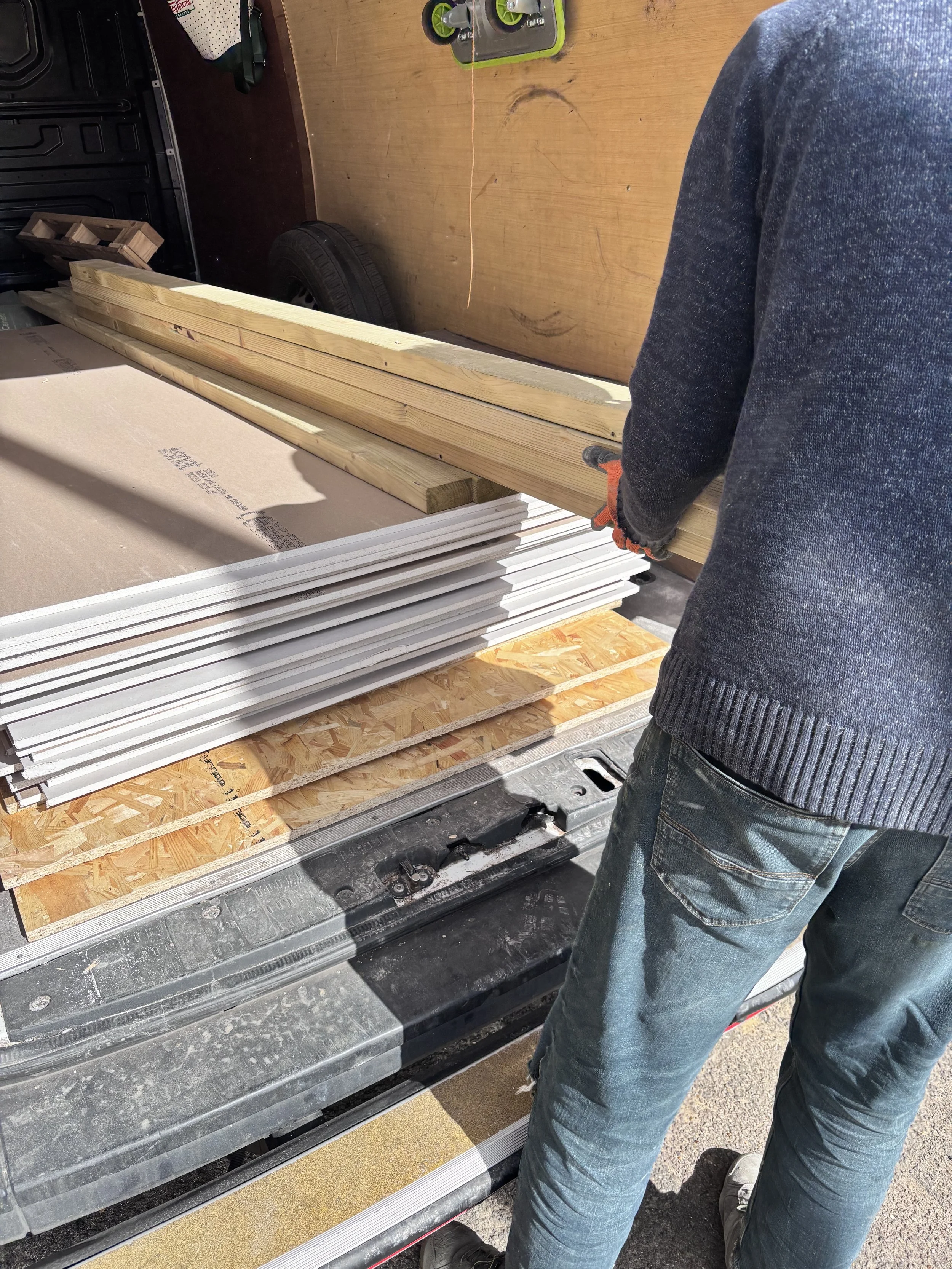A person in jeans and a sweater stacking wooden planks on a flatbed trailer.