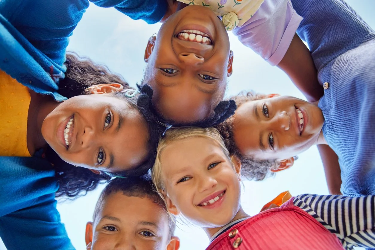 Children forming a circle with their heads together, smiling and looking down at the camera. All receive school speech therapy services provided by a contract speech therapist in Seattle, WA.