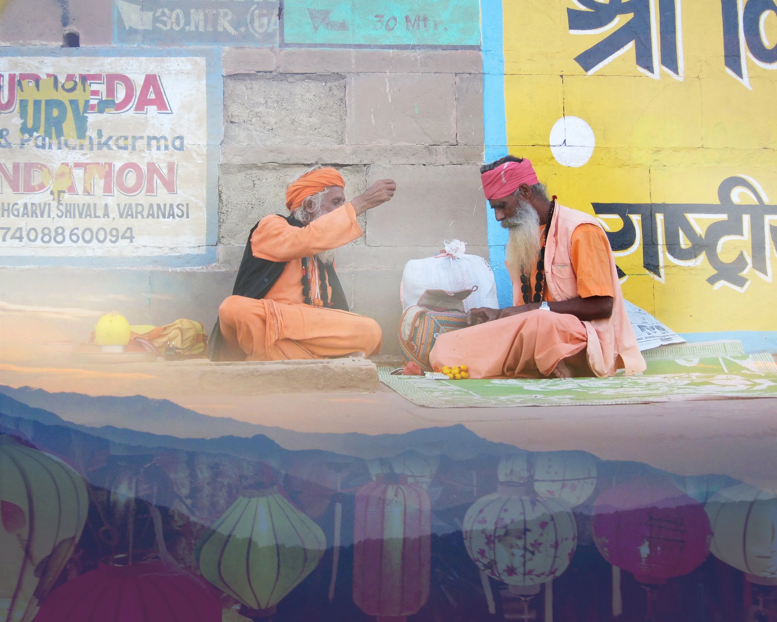 Two men dressed in orange sitting on the ground in front of painted wall, engaging in a conversation with a small white bag and small yellow objects nearby.