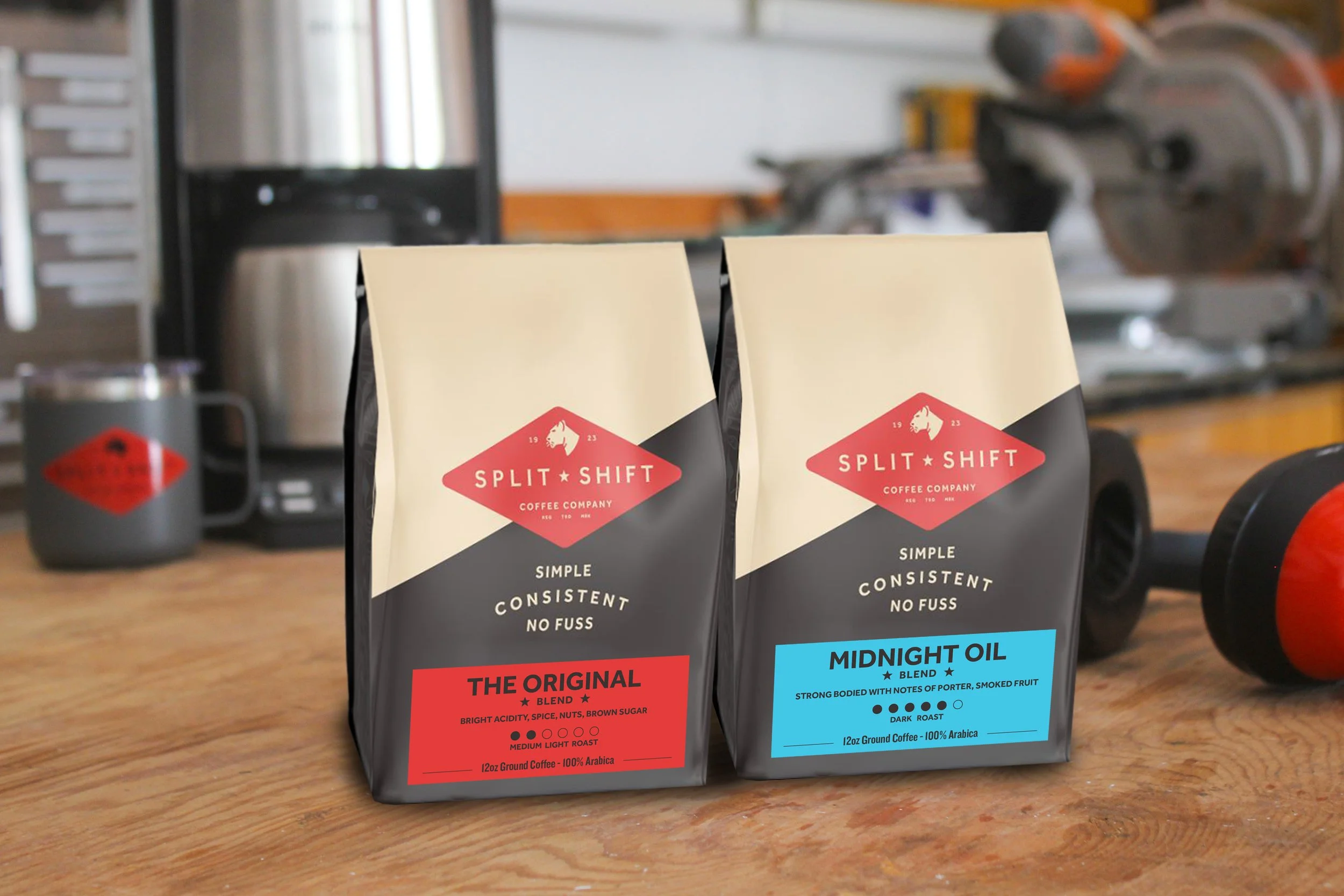 Two bags of Split Shift Coffee Company coffee on a wooden surface with industrial kitchen equipment in the background. One bag labeled 'The Original' with notes of brown sugar, spices, and nuts, and a medium roast. The other bag labeled 'Midnight Oil Blend' with notes of smoked fruit, dark roast, and 100% Arabica beans.