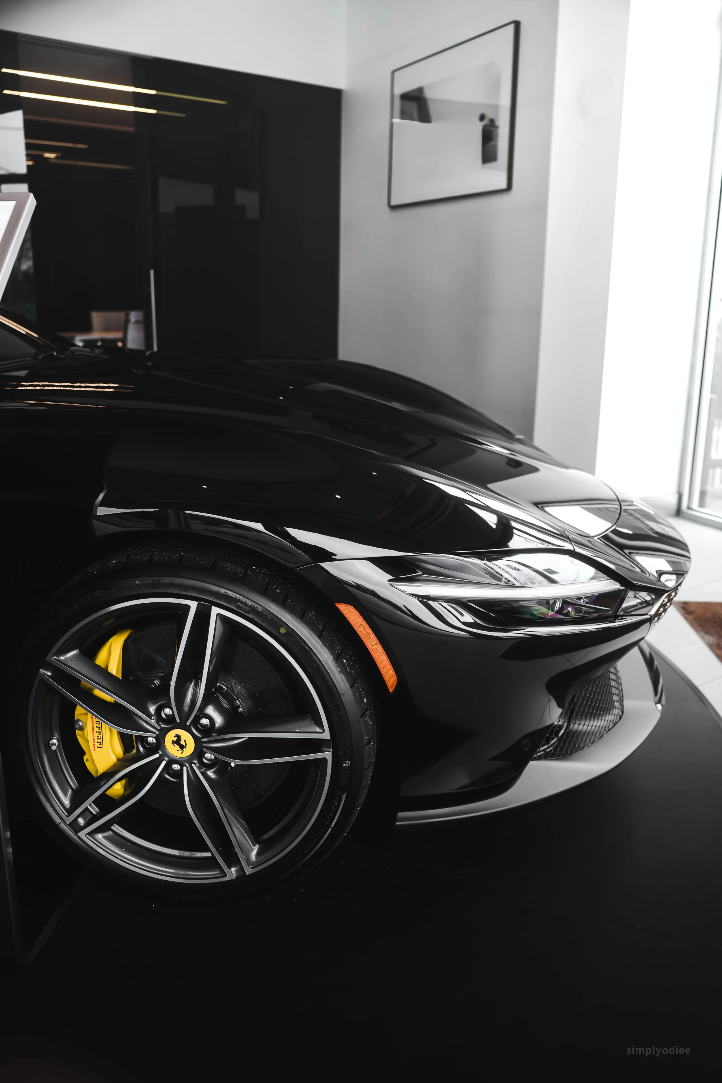 Close-up of a black Ferrari sports car with yellow brake calipers, on display indoors near a window.