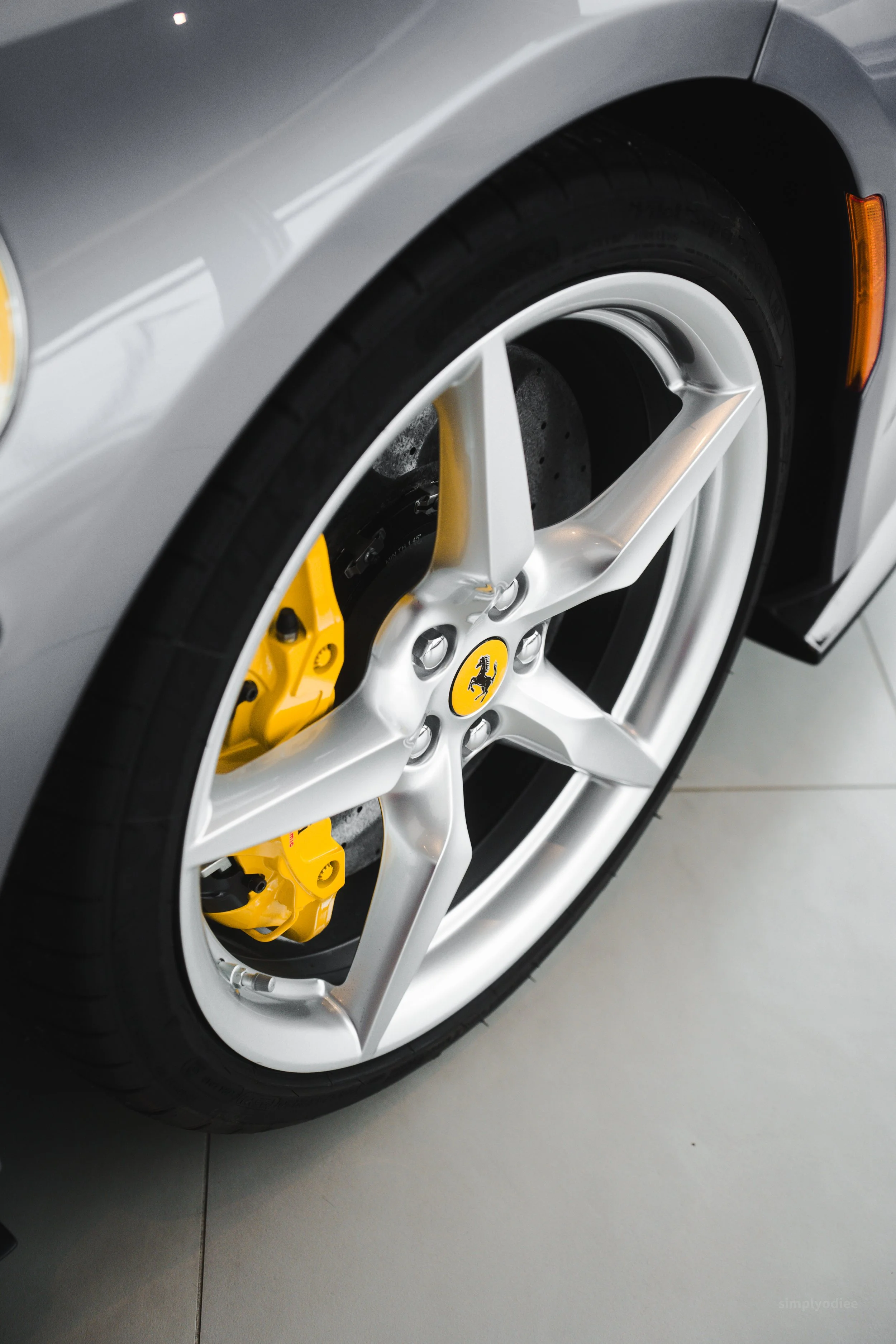 Close-up of a silver Ferrari wheel with yellow brake caliper and brake pad, featuring a Ferrari logo center cap.