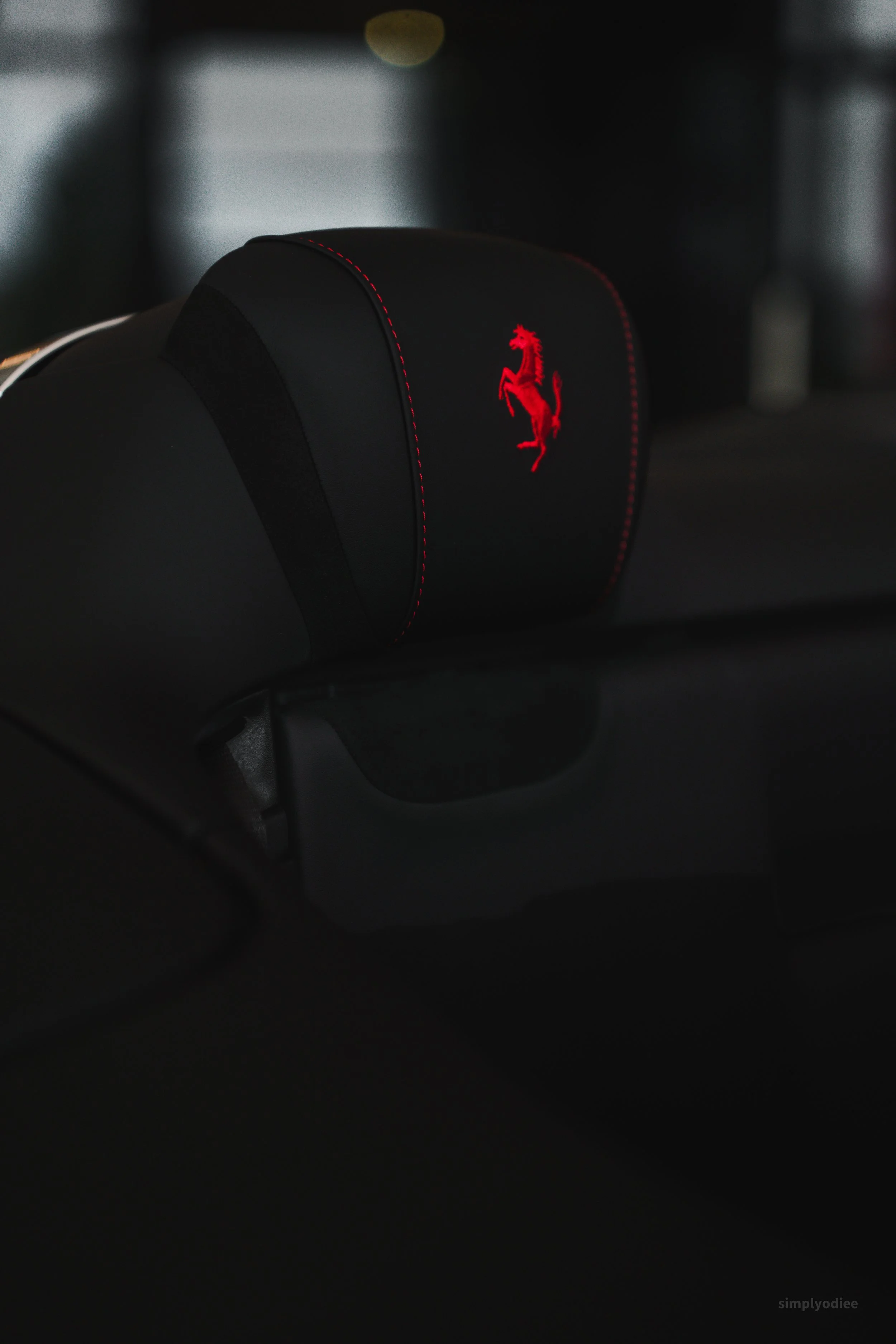 Close-up view of a car's headrest with the Ferrari logo illuminated in red, set in a dark environment.