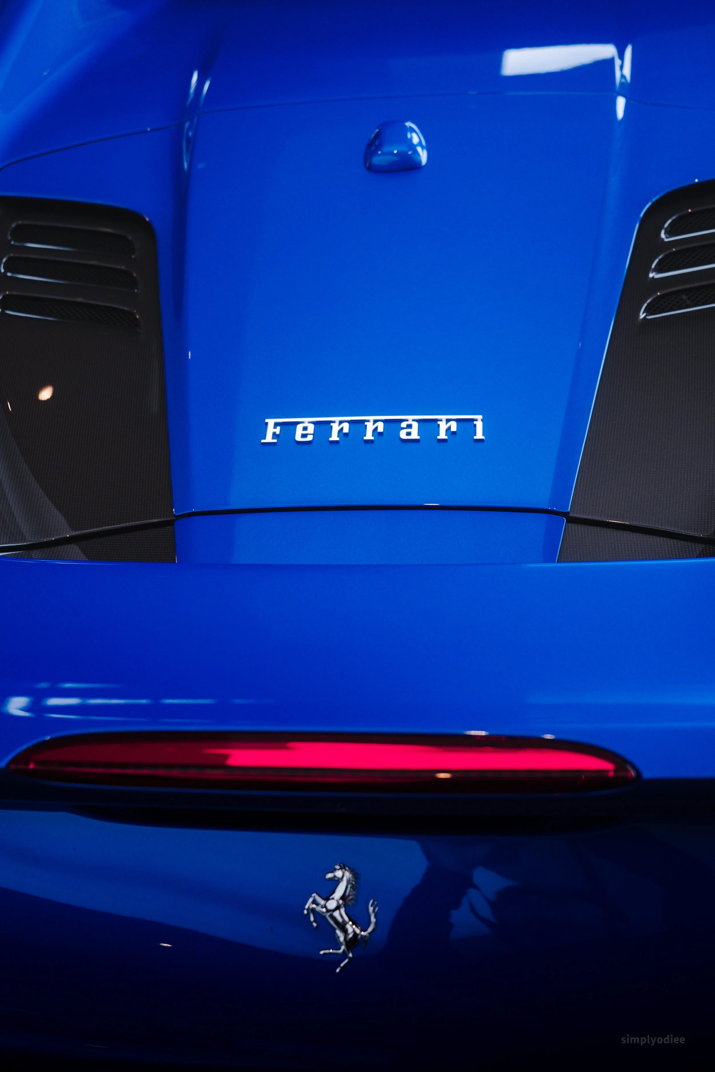 Close-up of the front hood of a blue Ferrari sports car, featuring the Ferrari logo and emblem.