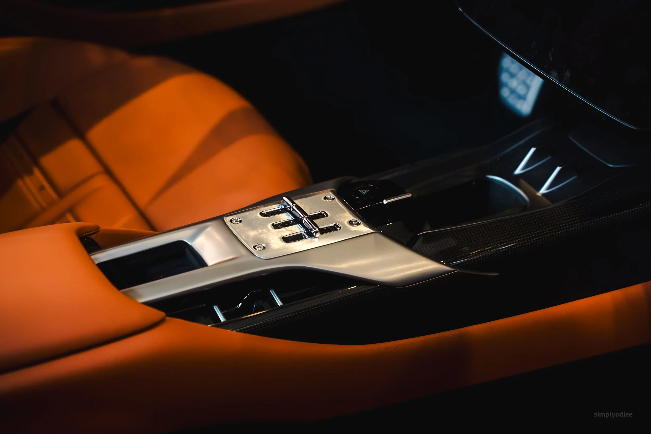 Close-up of the center console and gear shifter of a luxury sports car with orange leather interior and carbon fiber accents.