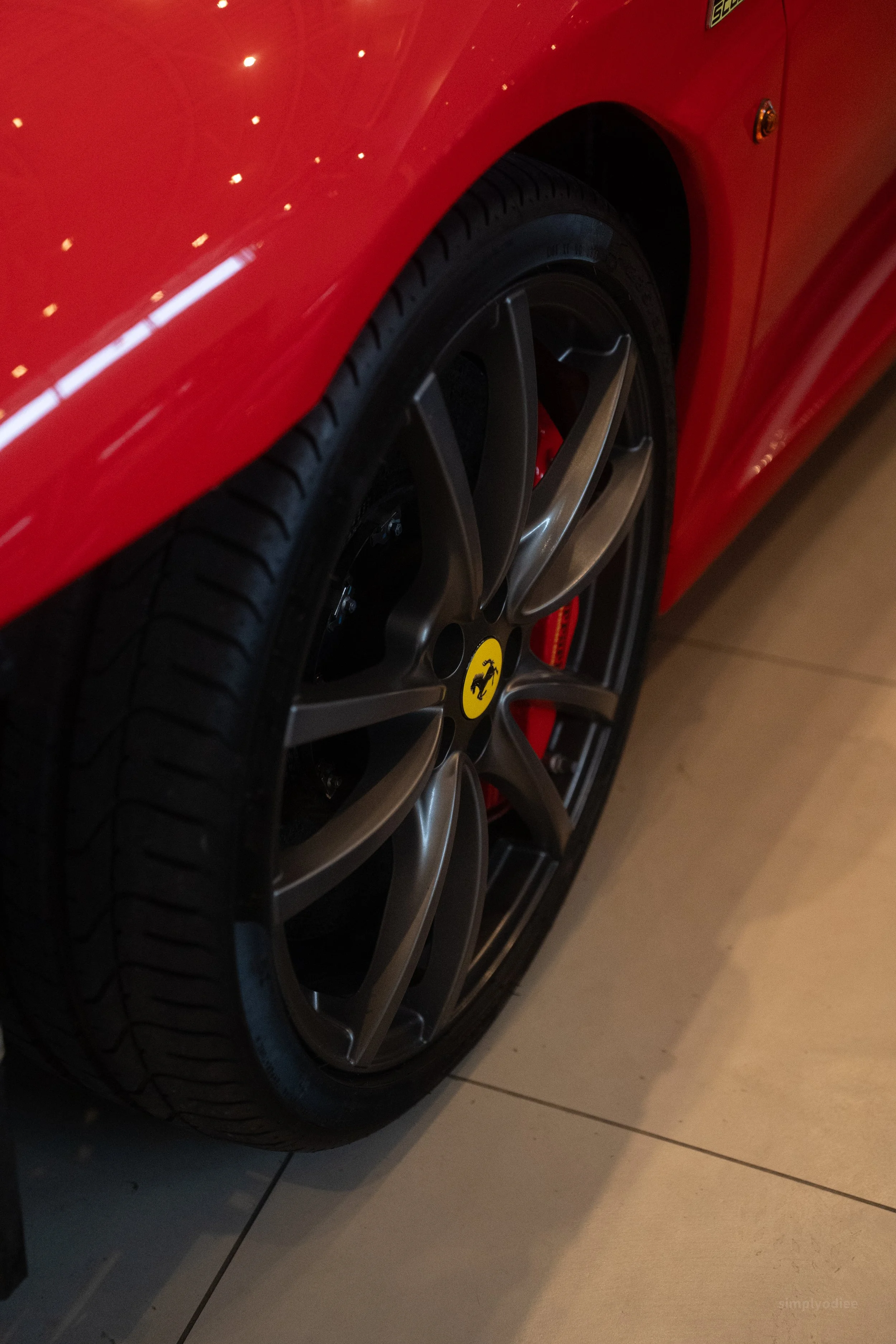Close-up of a red Ferrari sports car's wheel with a black tire and alloy rim, featuring the Ferrari logo at the center.