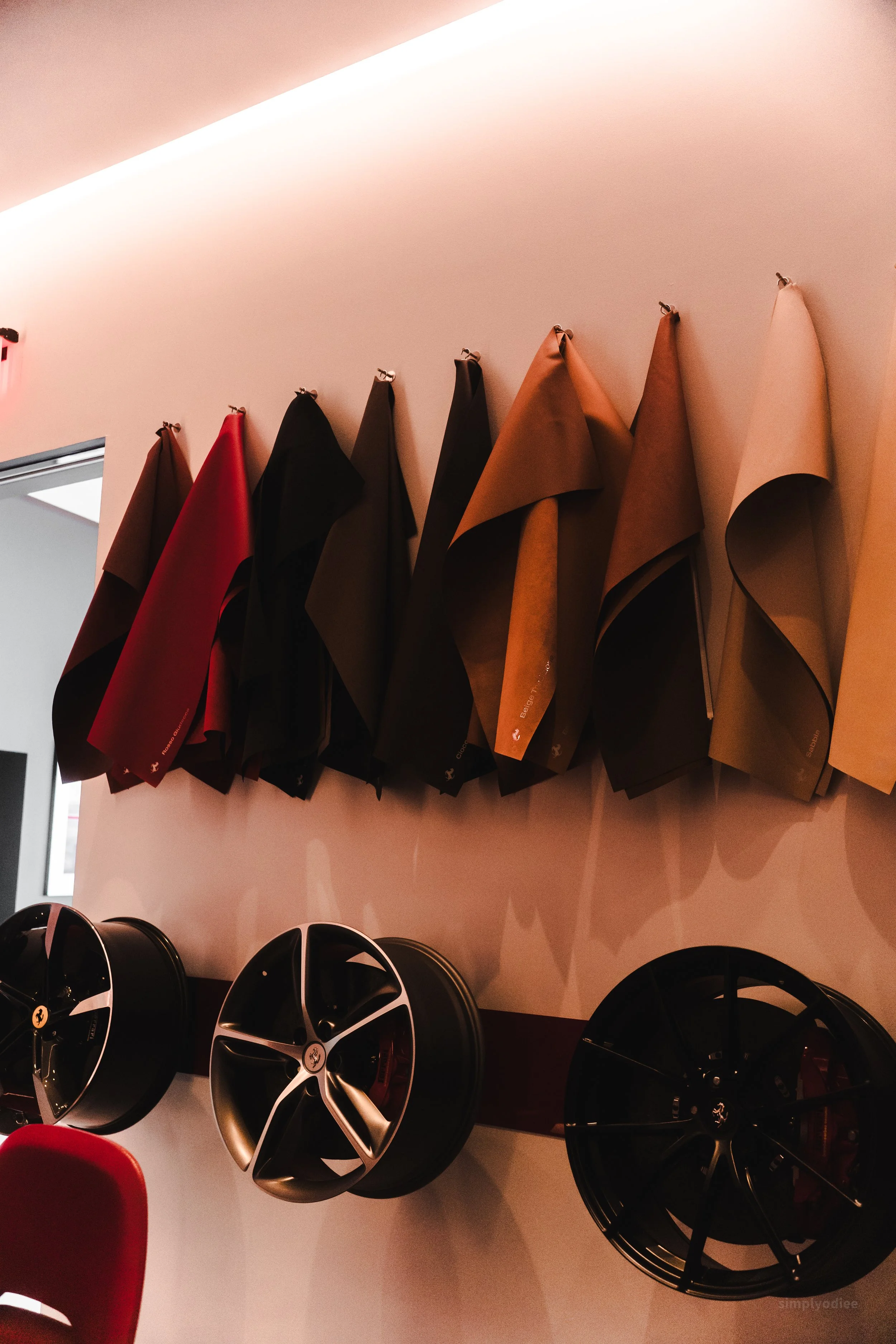Rows of leather or synthetic material samples in various colors hanging on a wall, with car rims displayed below.