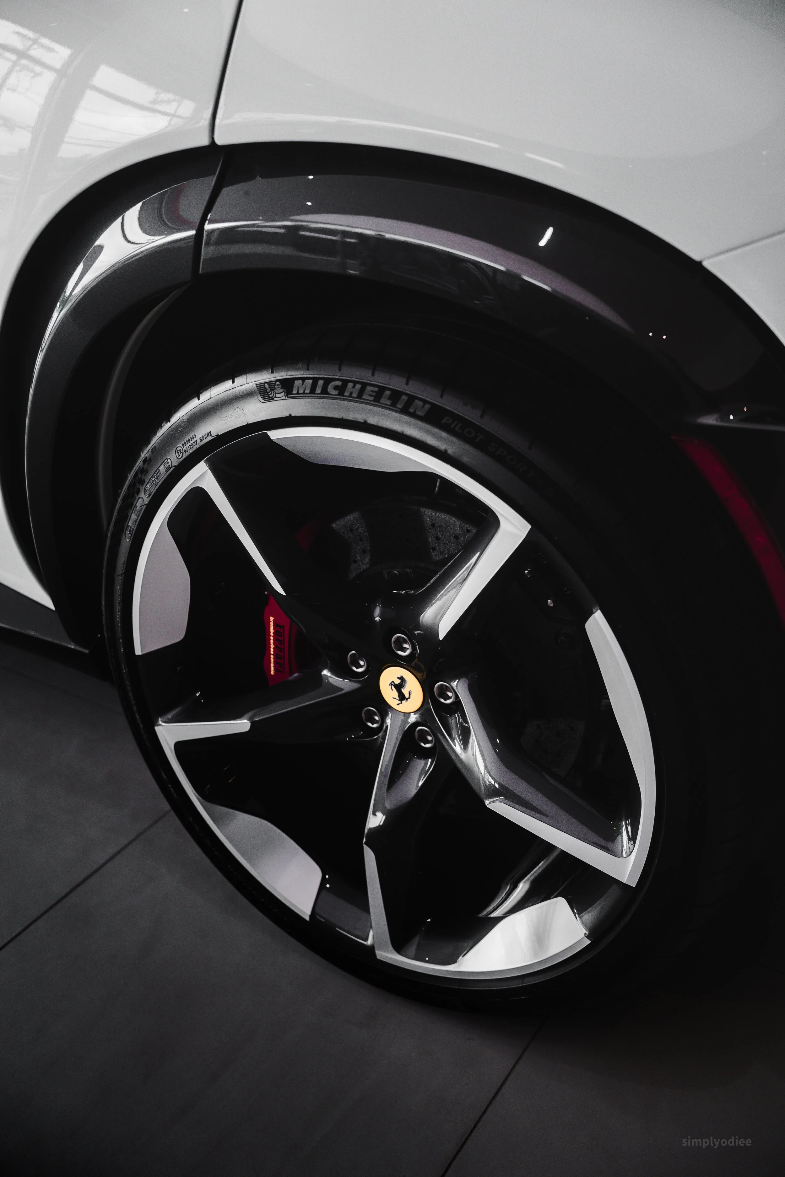 Close-up of a Tesla car wheel with Michelin Pilot Sport tire, red brake caliper, and Ferrari emblem on the center cap.