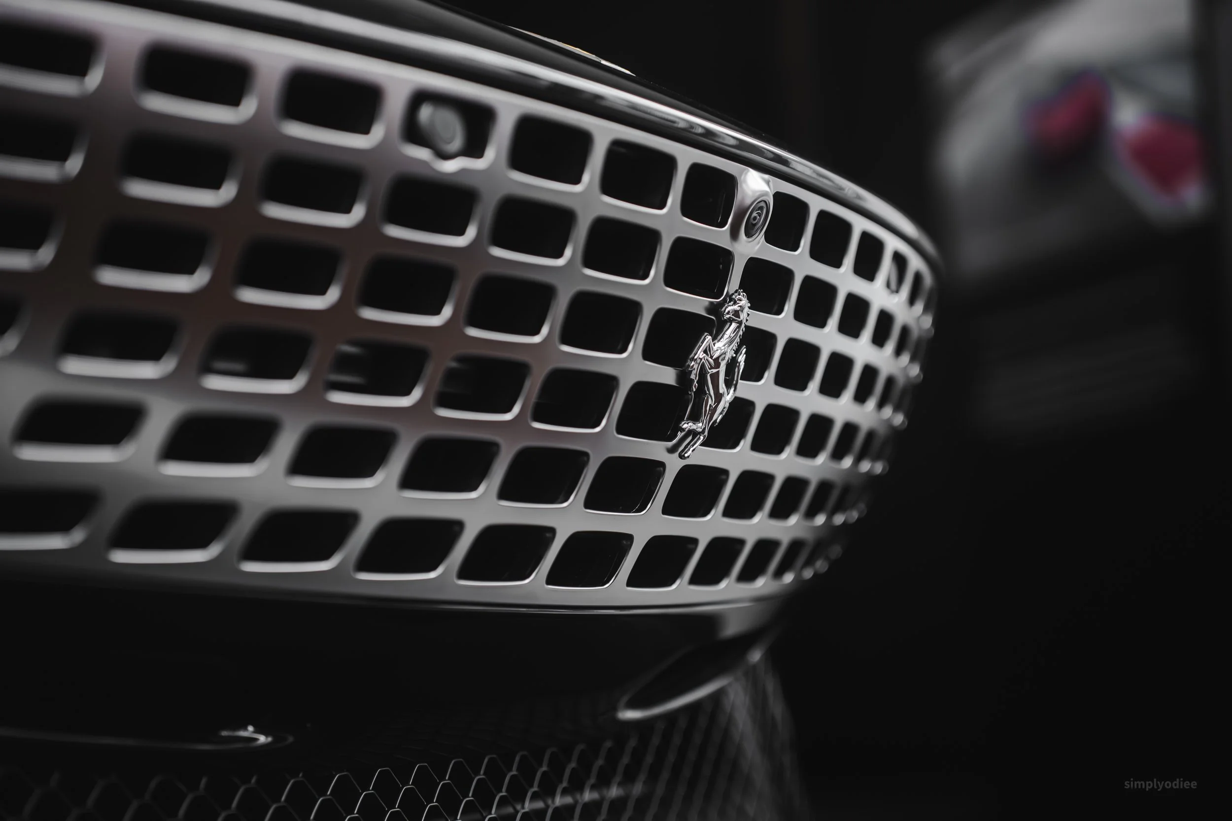Close-up of a front grille of a black luxury car with a silver logo of a jumping horse in the center, highlighting the grille's grid pattern.