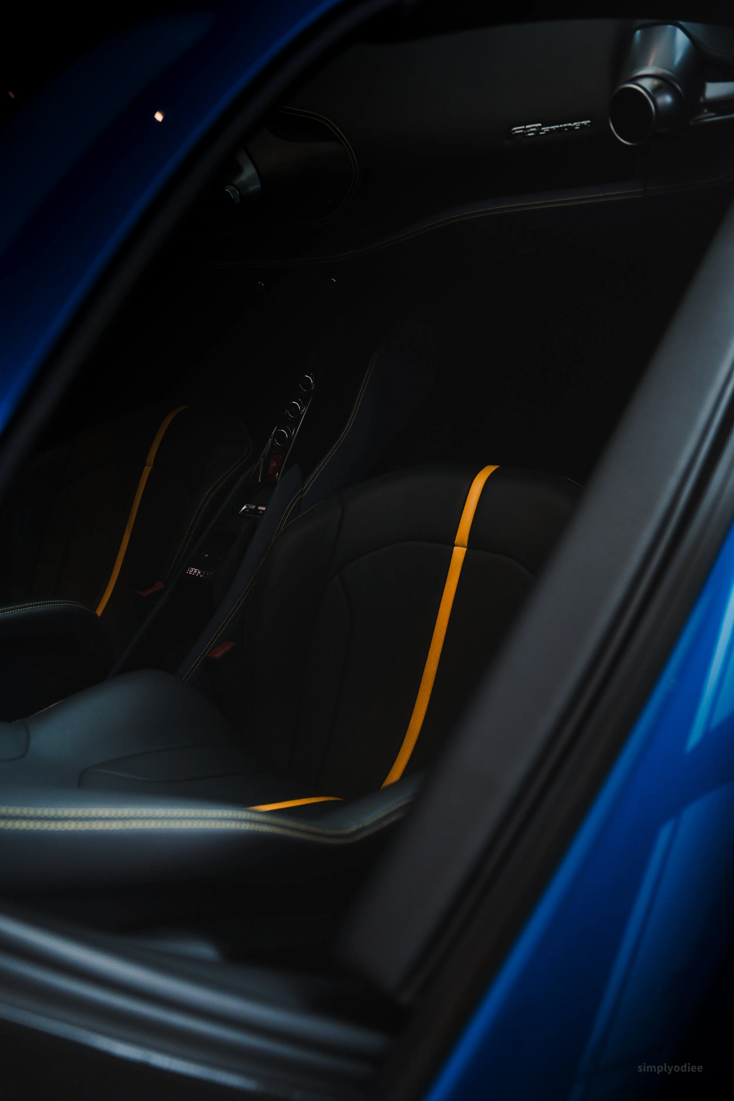 The interior of a blue sports car showing black seats with yellow stripe accents and a partial view of the dashboard.