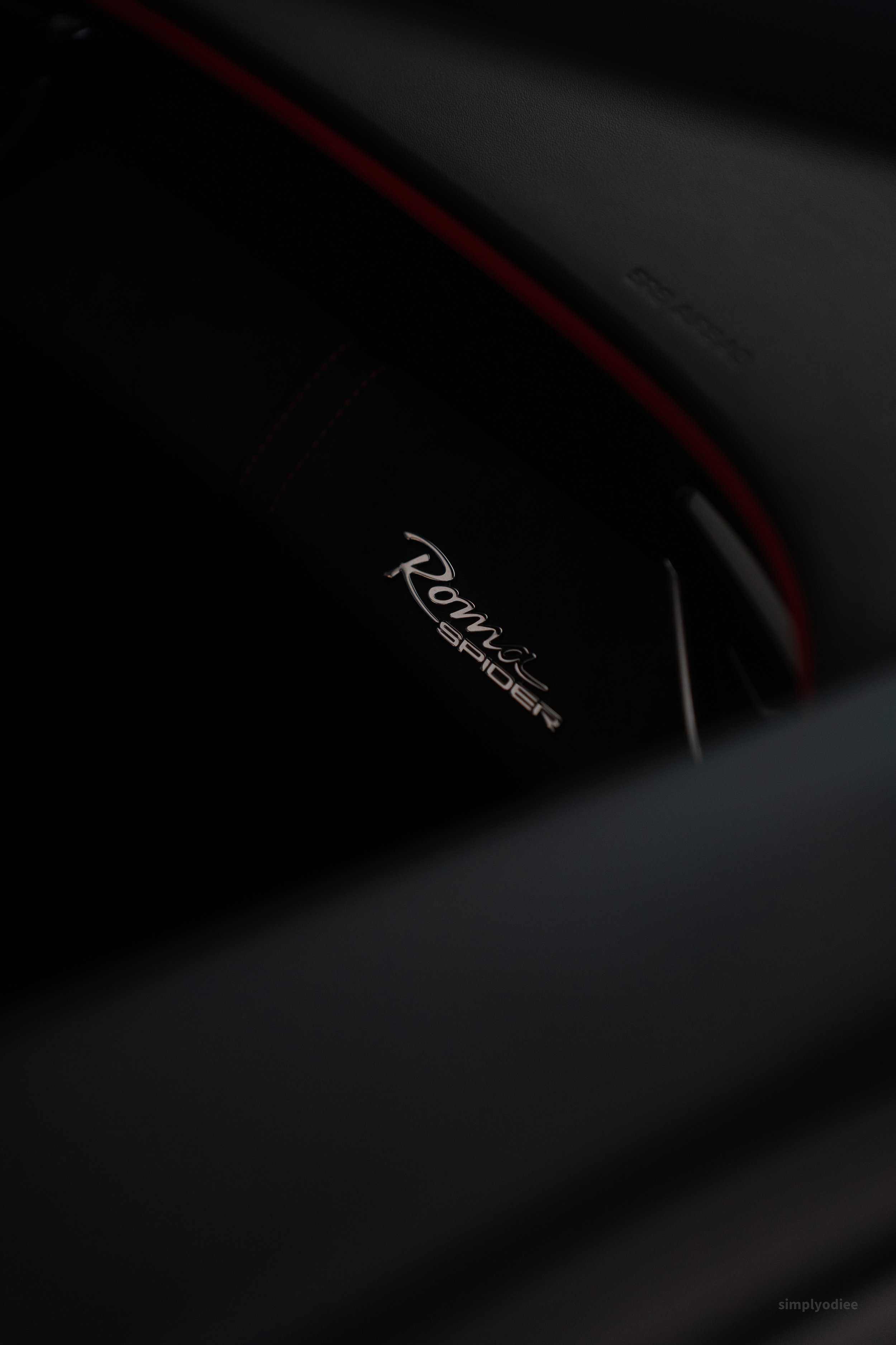 Close-up of a black car interior with a chrome emblem that says 'Romeo SPIDER' and a red trim detail.