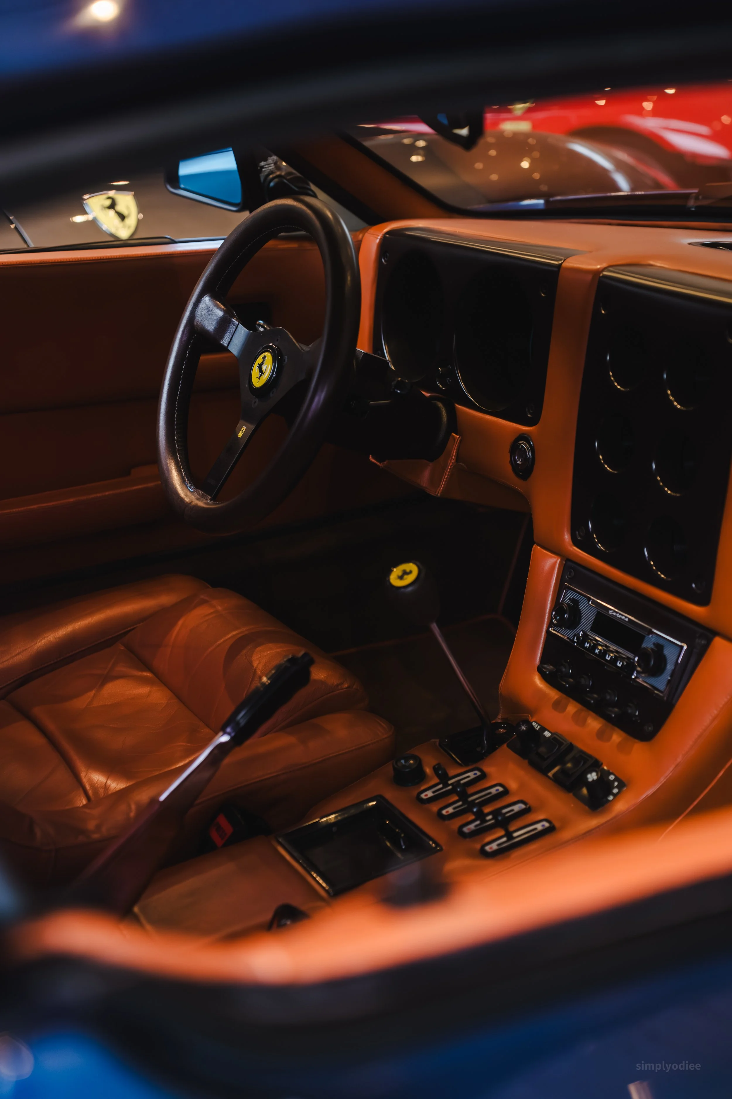 Interior of a vintage Ferrari sports car with tan leather seats, a black steering wheel with the Ferrari logo, and a tan dashboard with various controls and gauges.