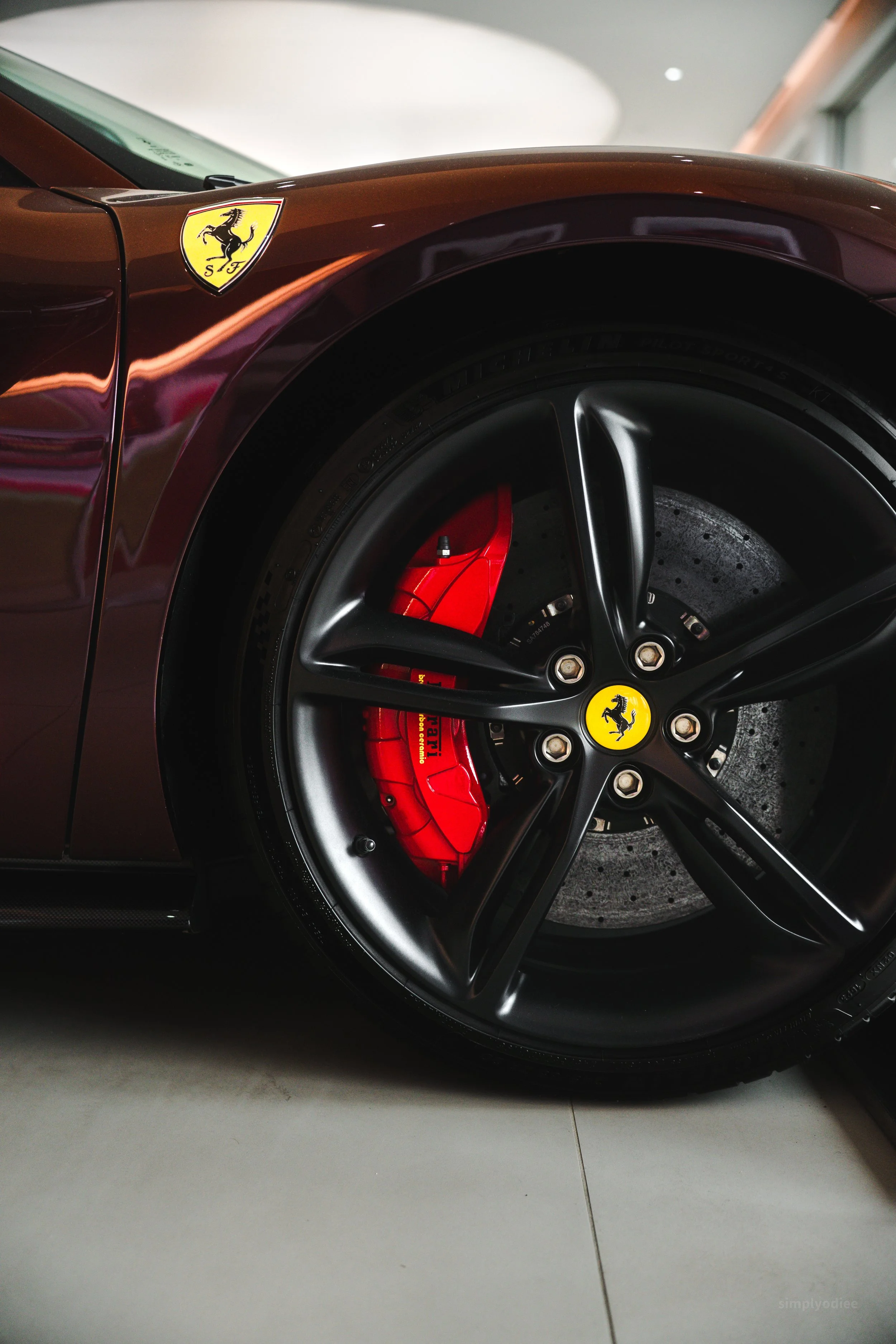 Close-up of a Ferrari sports car wheel with a red brake caliper and black rim, featuring the Ferrari logo on the center cap and on a badge on the car's body.