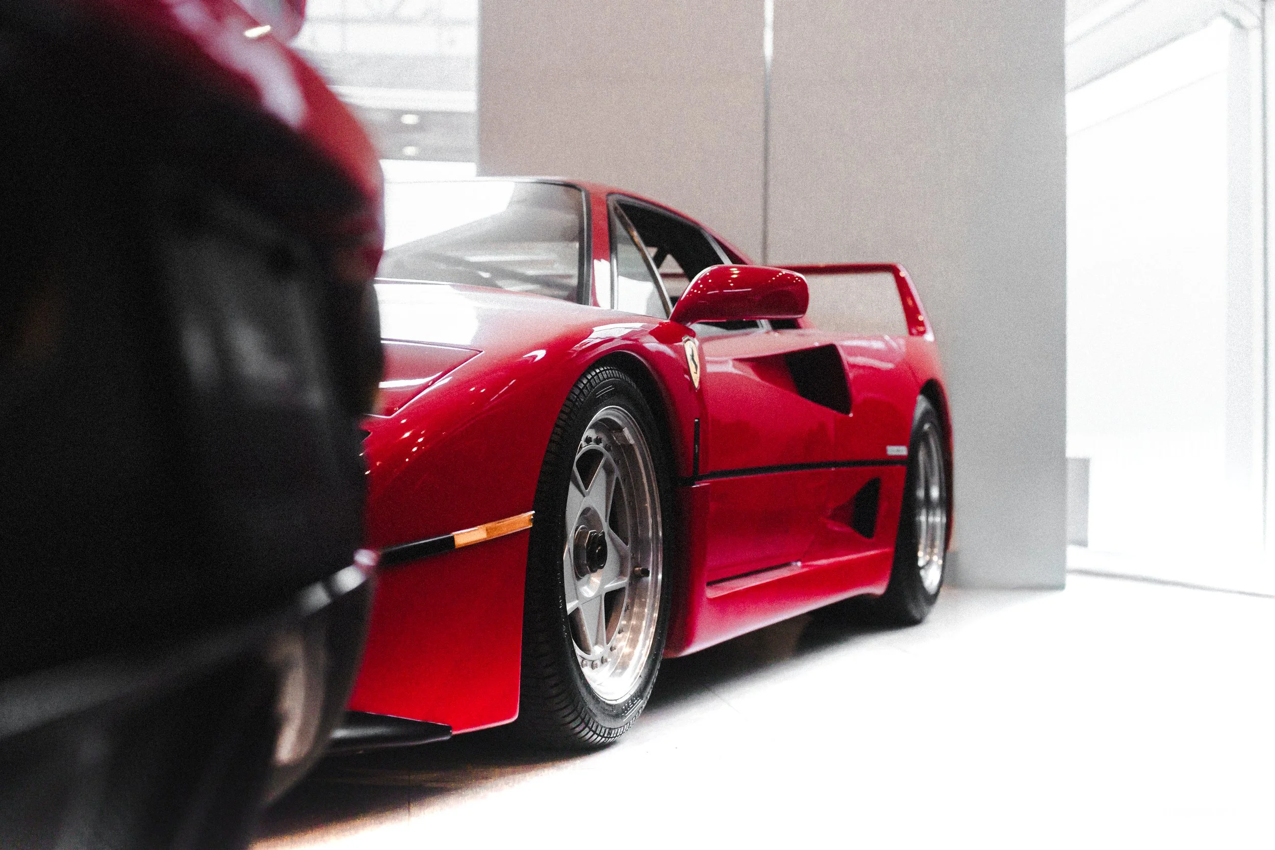 A red Ferrari sports car on display indoors, viewed from a low angle near the front left side.