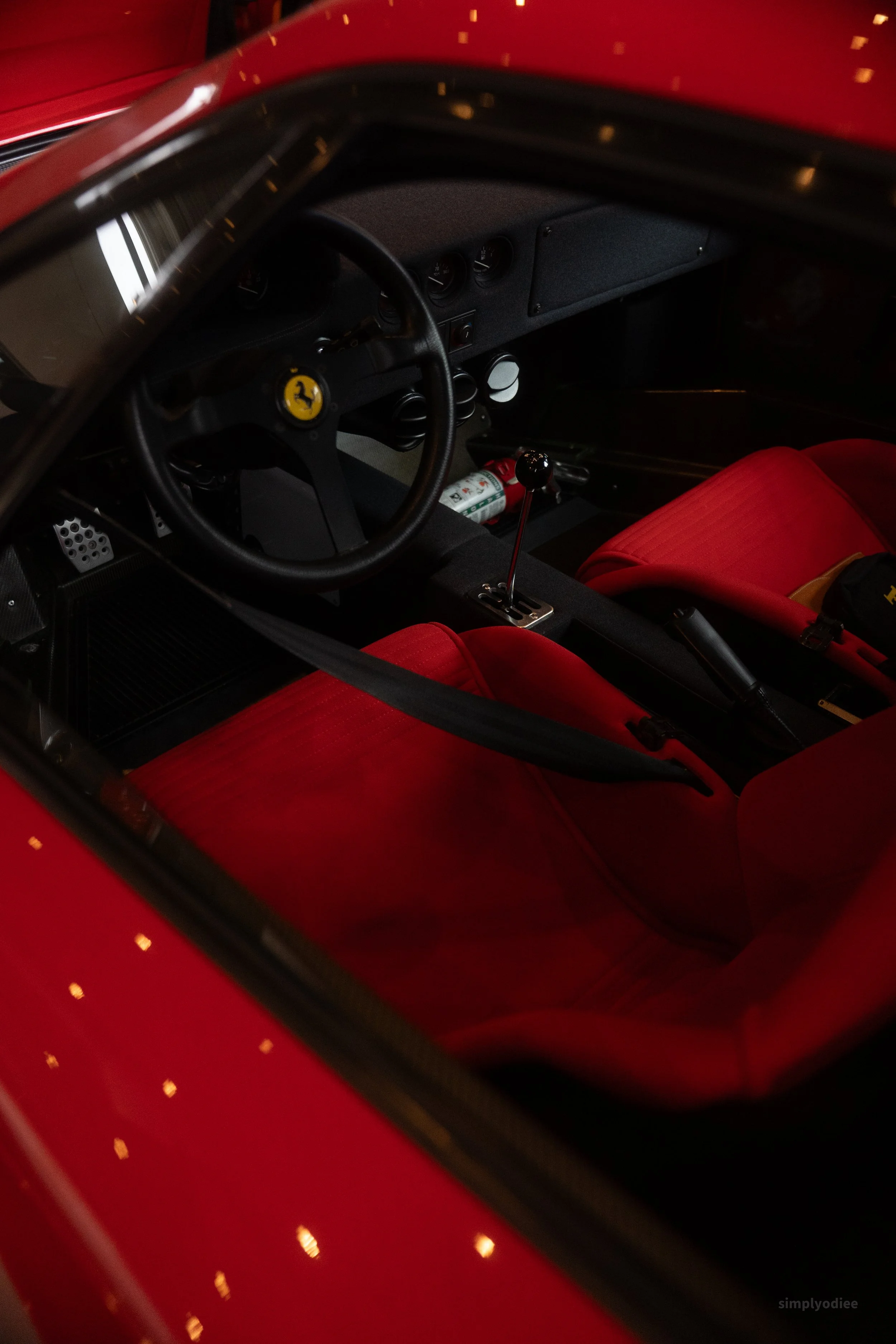 Interior of a red race car with red bucket seats, a black steering wheel with a Ferrari emblem, and a gear shift.