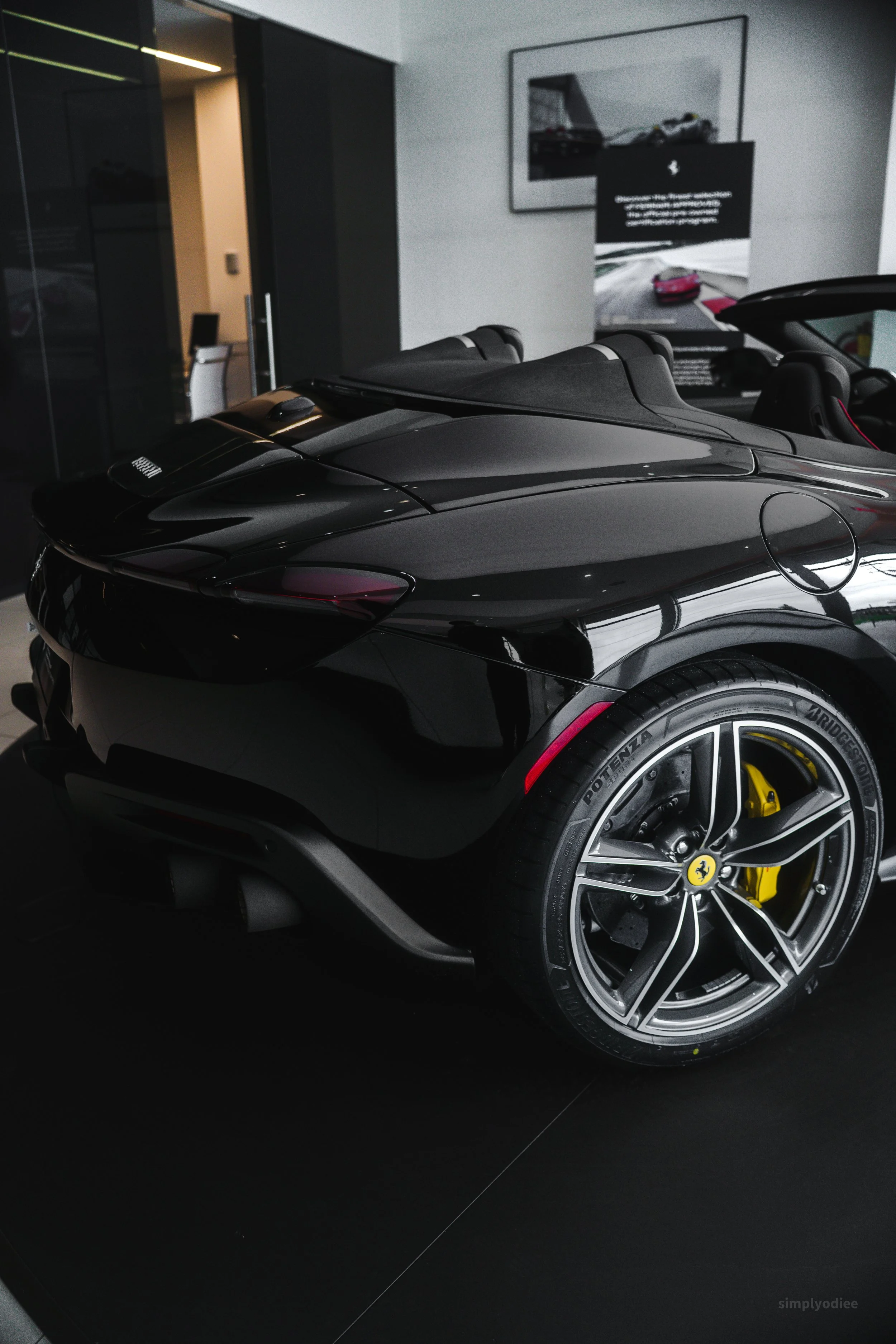 Black convertible sports car with yellow brake calipers inside a modern showroom.