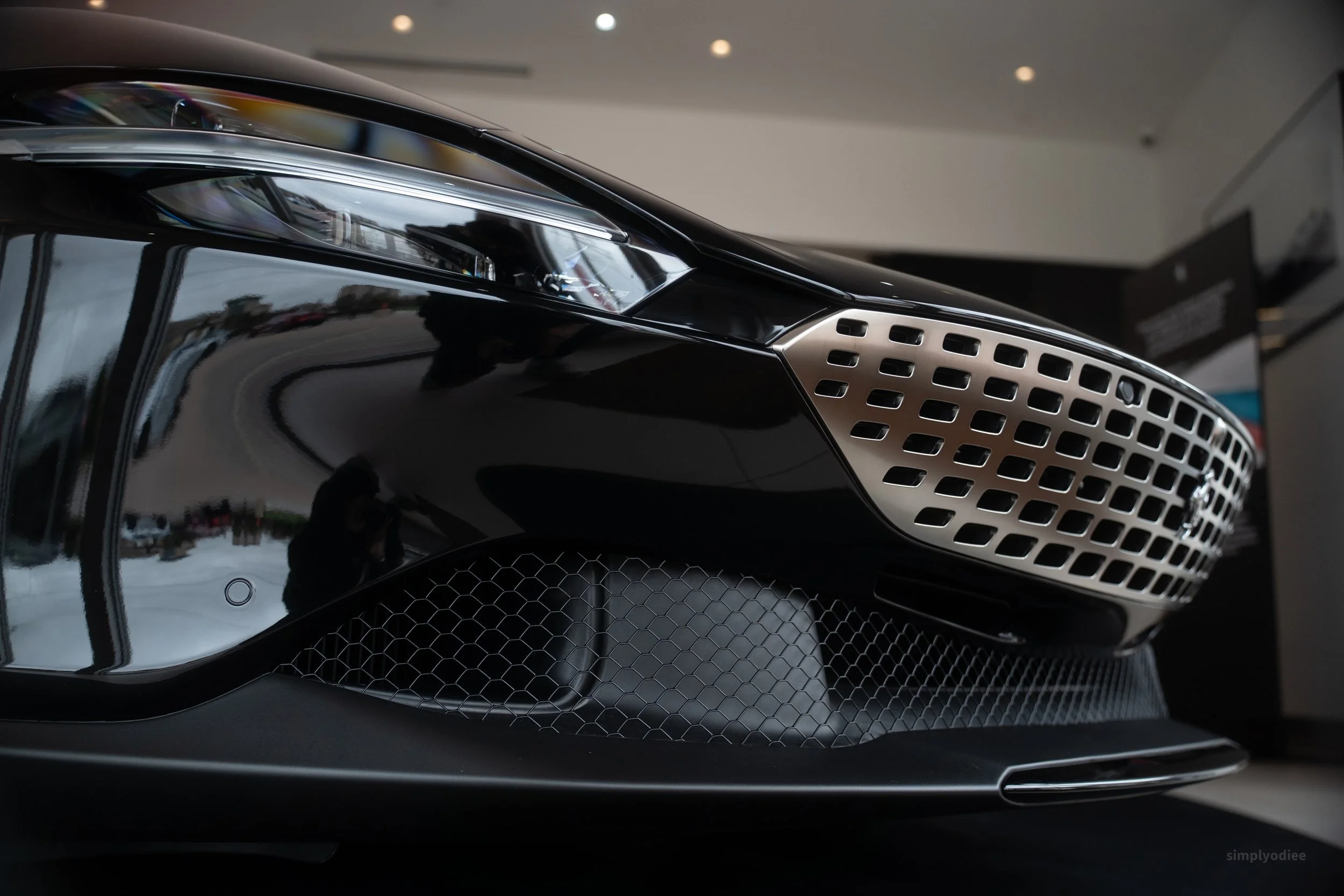 Close-up of a black luxury car's front end, showing the headlight, grille, and air intake with a reflective glossy surface.