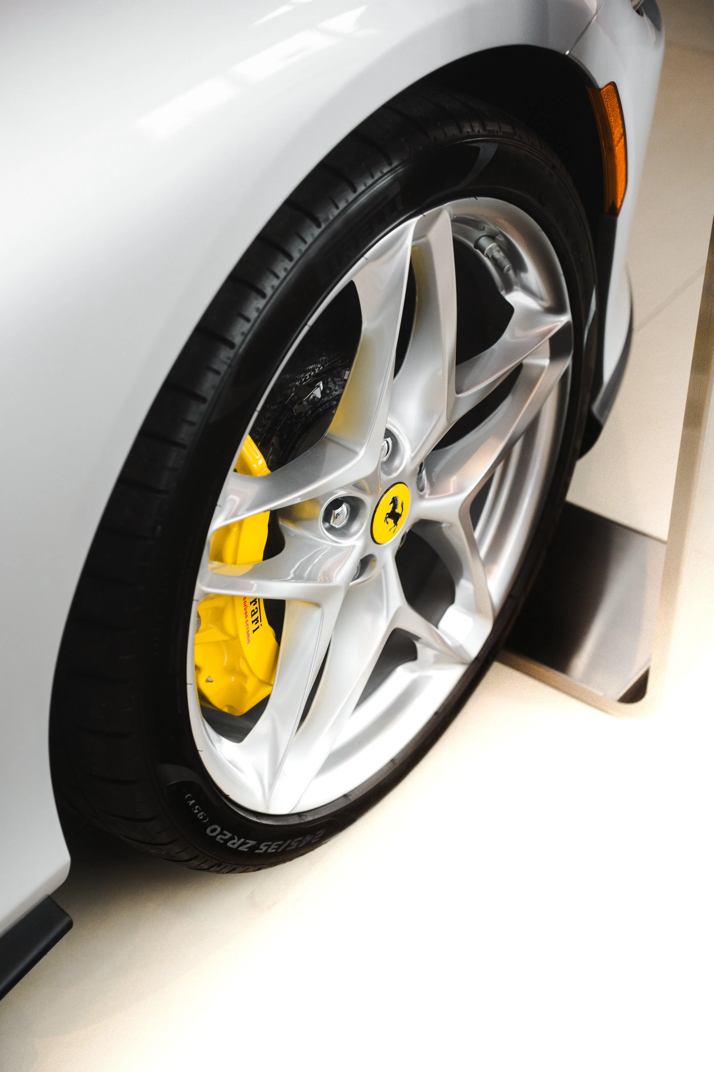 Close-up of a silver Ferrari car wheel with a yellow brake caliper and a black tire, showing the Ferrari logo on the wheel center cap.
