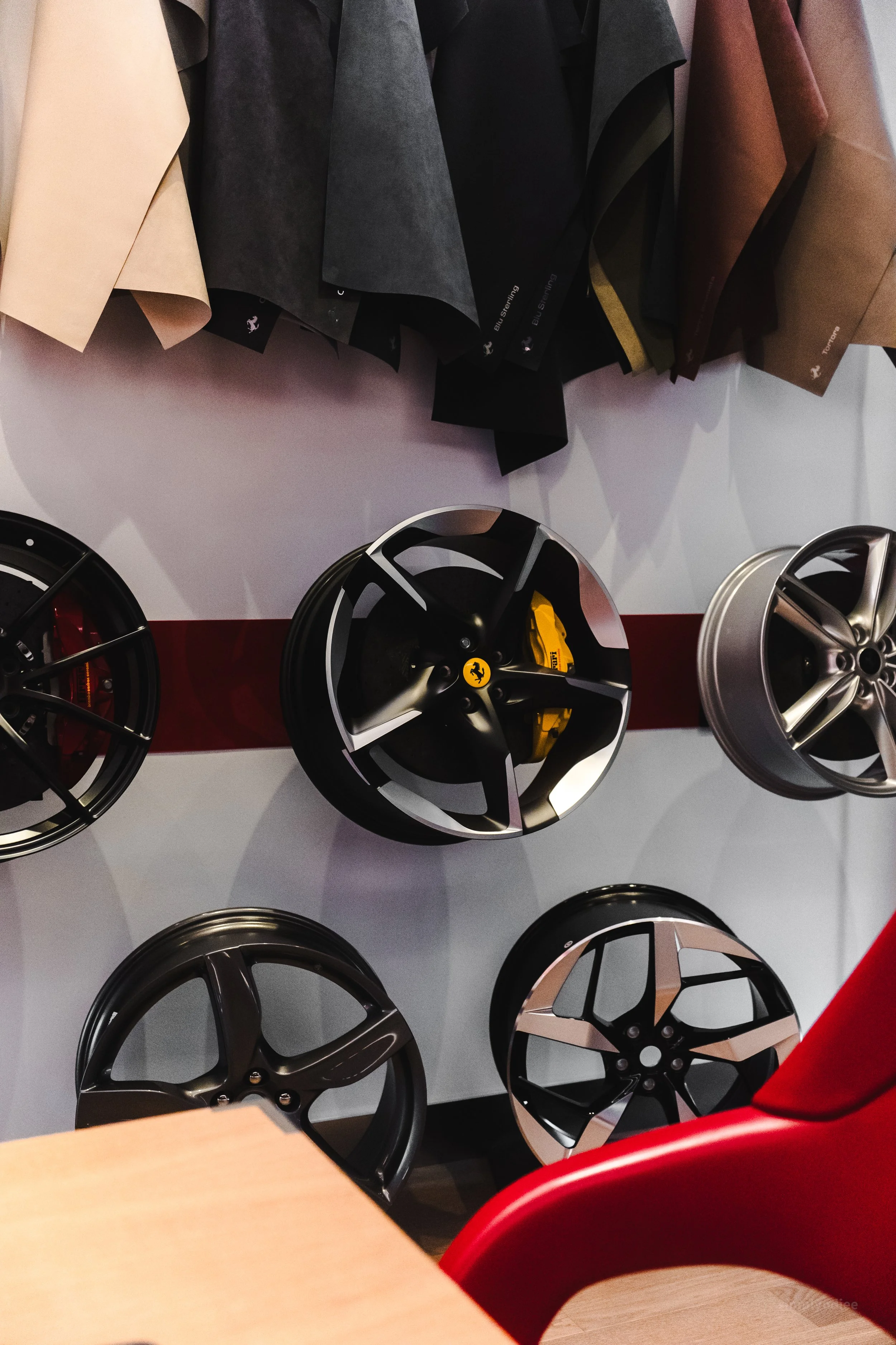 Display of five car wheels with various designs, mounted on a wall, with fabric samples hanging above.
