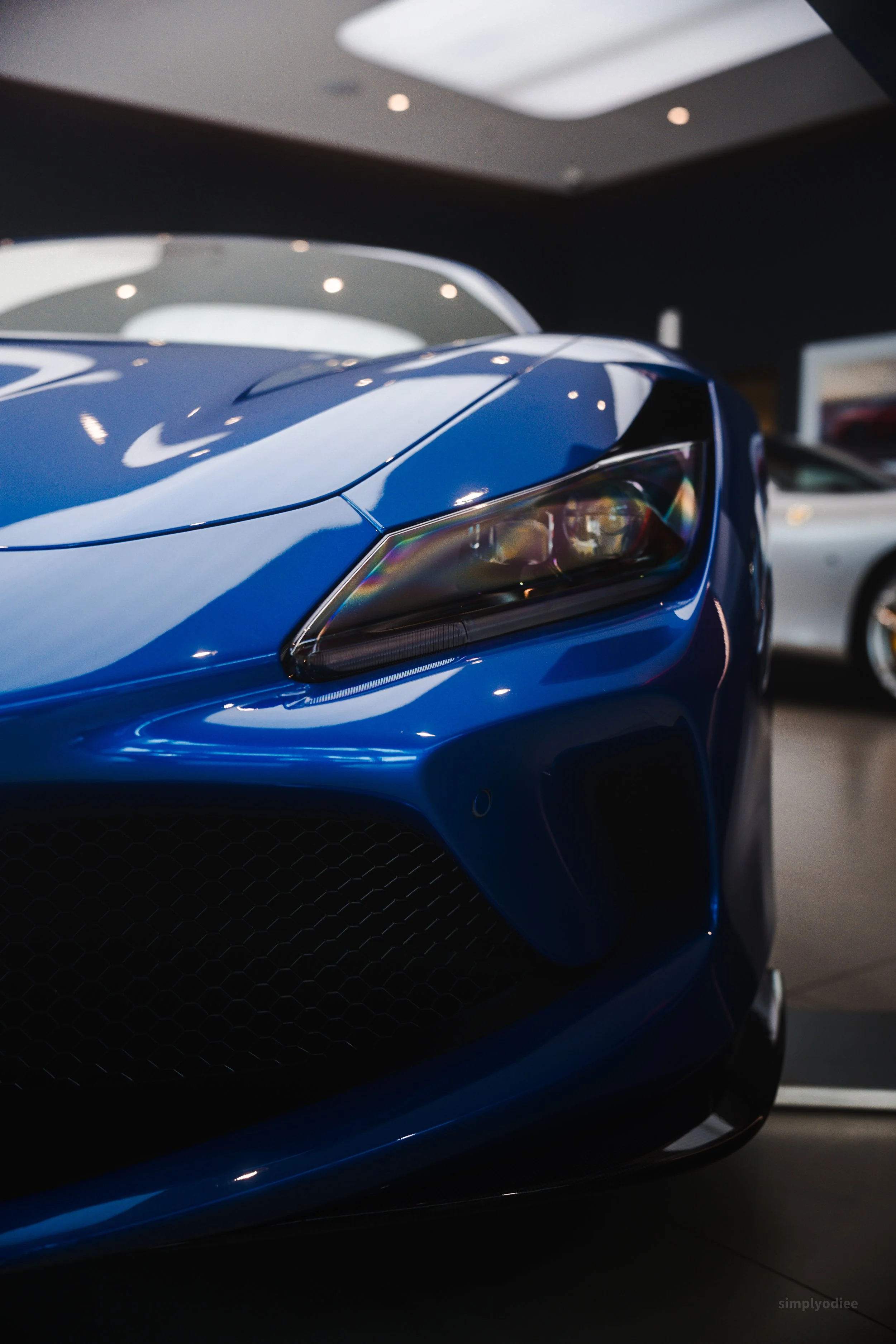Close-up of a blue sports car's front end, showing the headlight, grille, and sleek body.