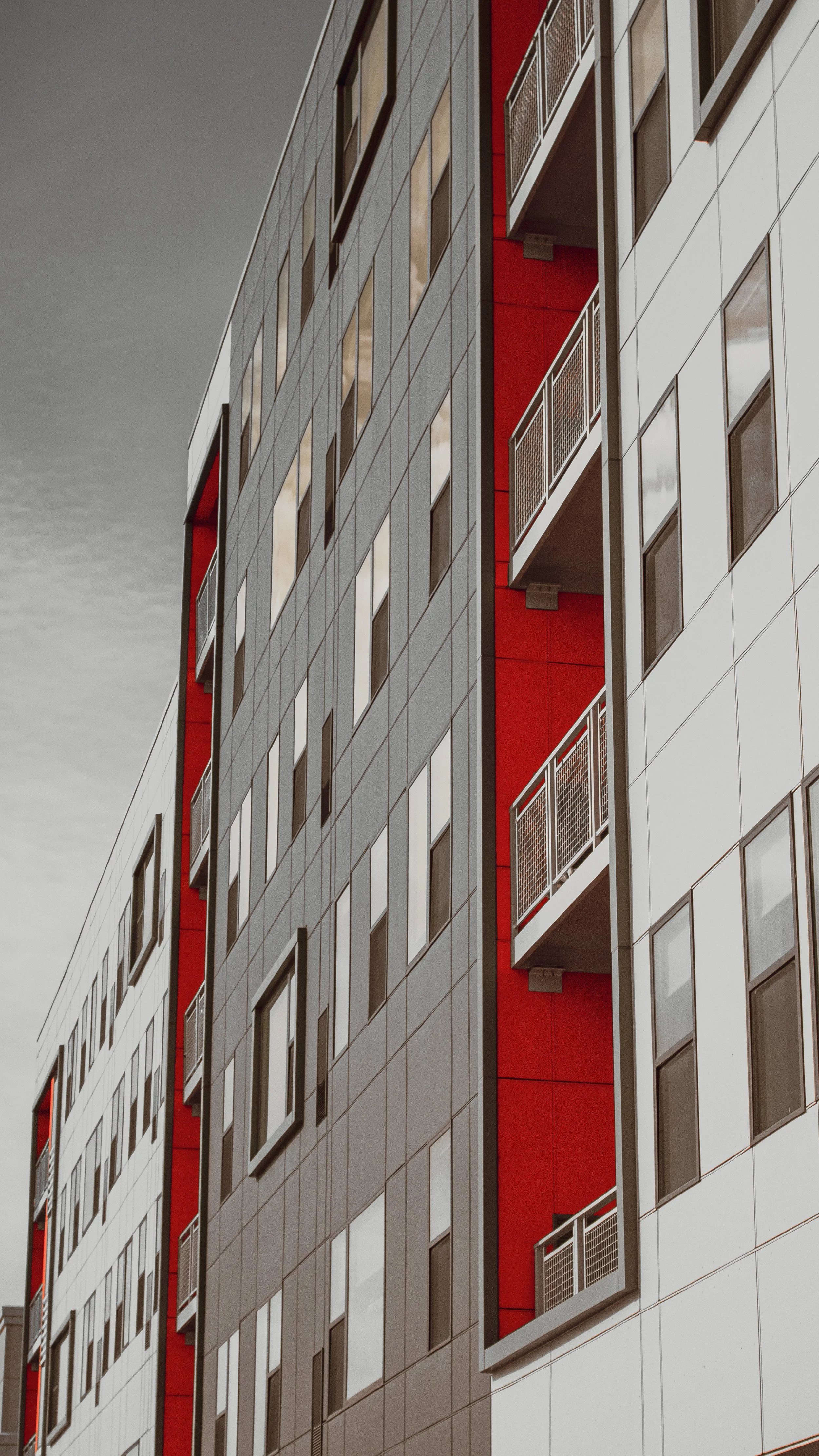 Modern multi-story apartment building with a geometric design, gray and white panels, and red accents on the balconies.