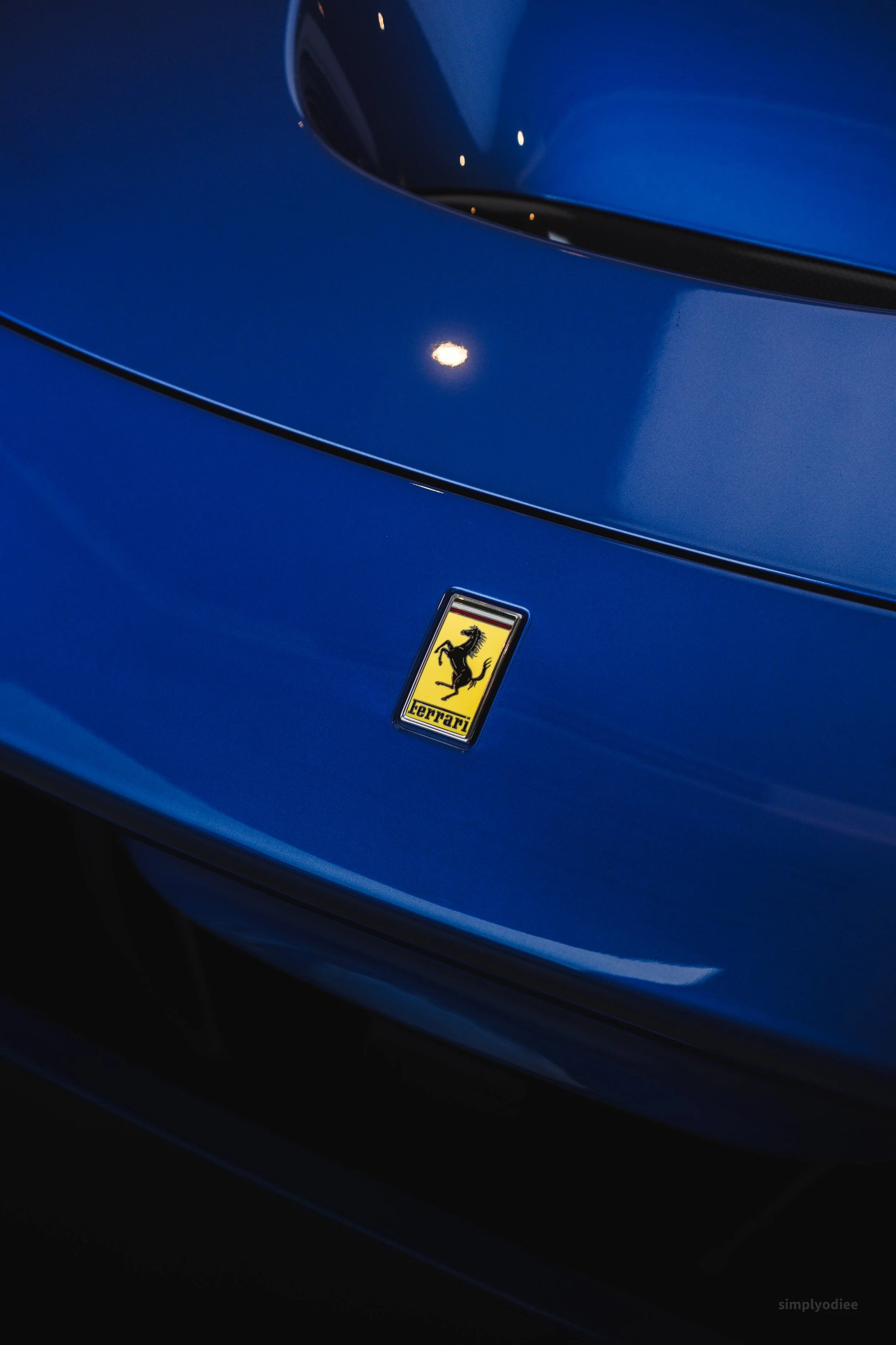 Close-up of the front part of a blue Ferrari car, showing the Ferrari emblem with a black prancing horse on a yellow shield.
