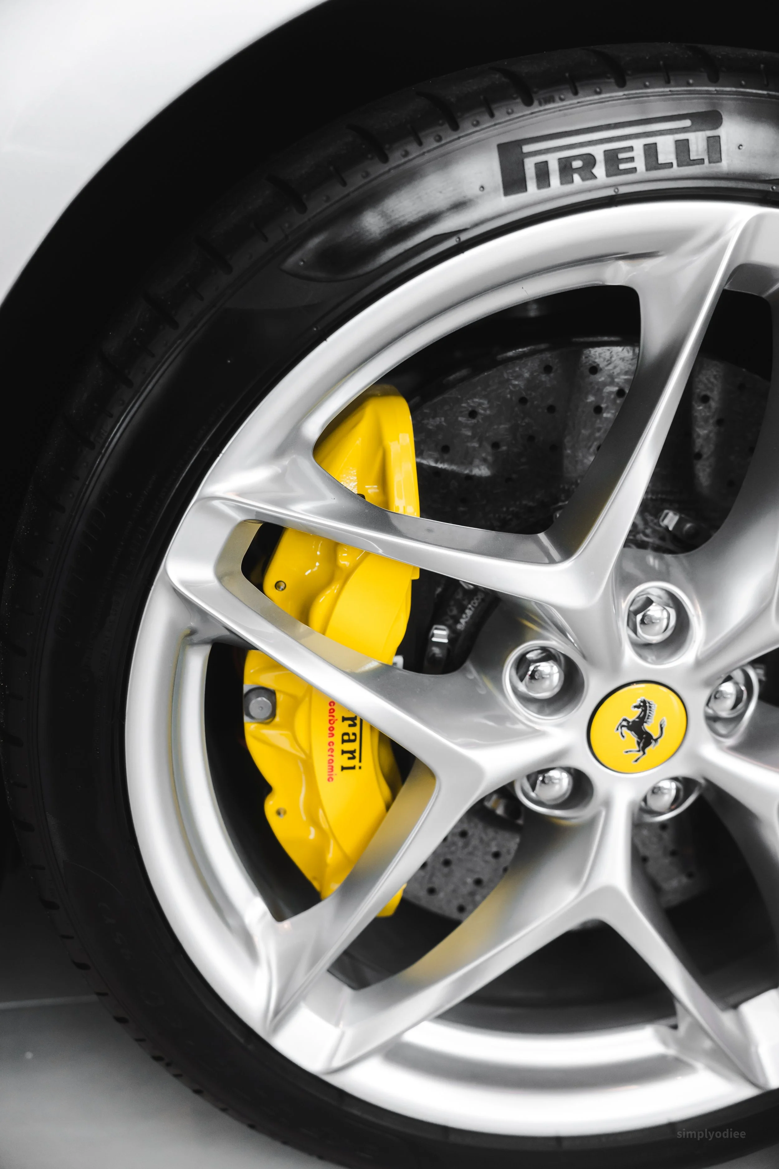 Close-up of a Ferrari wheel with a yellow brake caliper visible behind a silver alloy rim, and a black Pirelli tire.