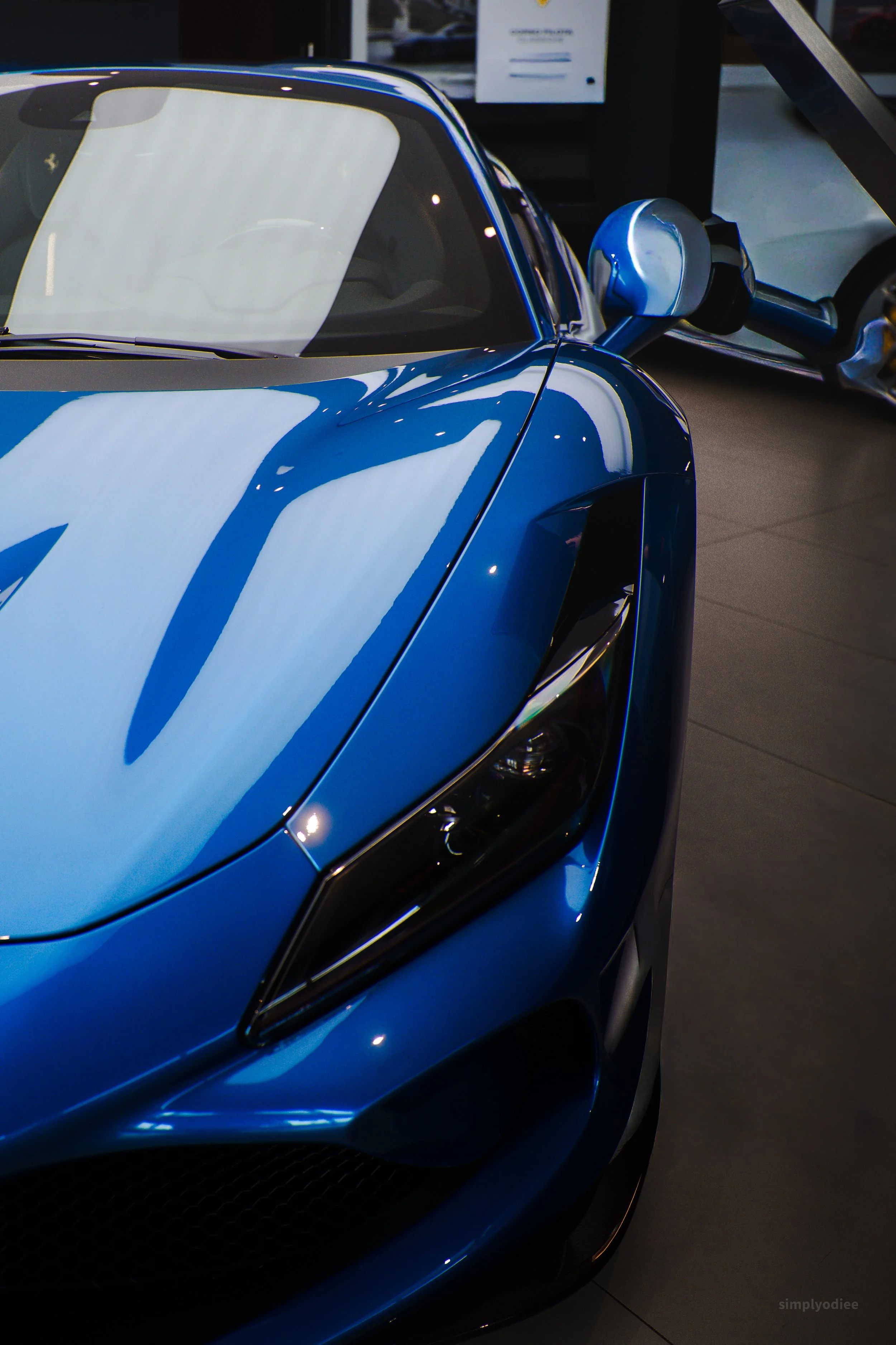 Close-up of a shiny blue luxury sports car on display indoors, with part of another vehicle in the background.