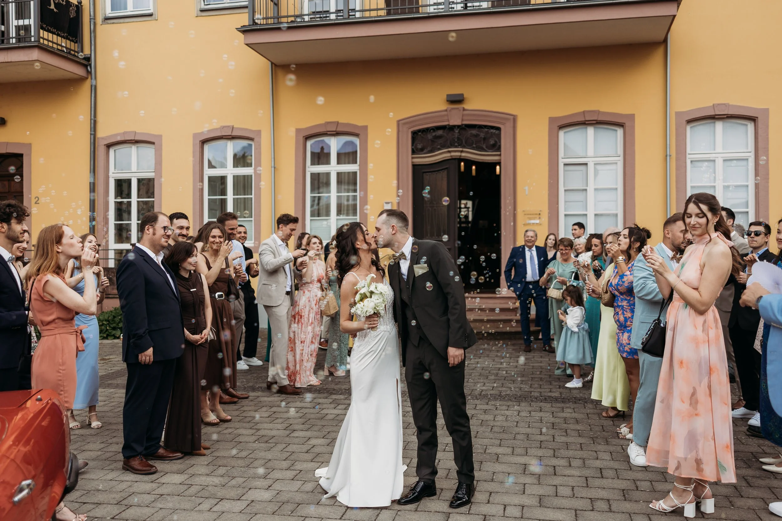 Ein Hochzeitsfest mit einem Brautpaar, das sich küsst, umgeben von Freunden und Familie vor dem Standesamt in Karben