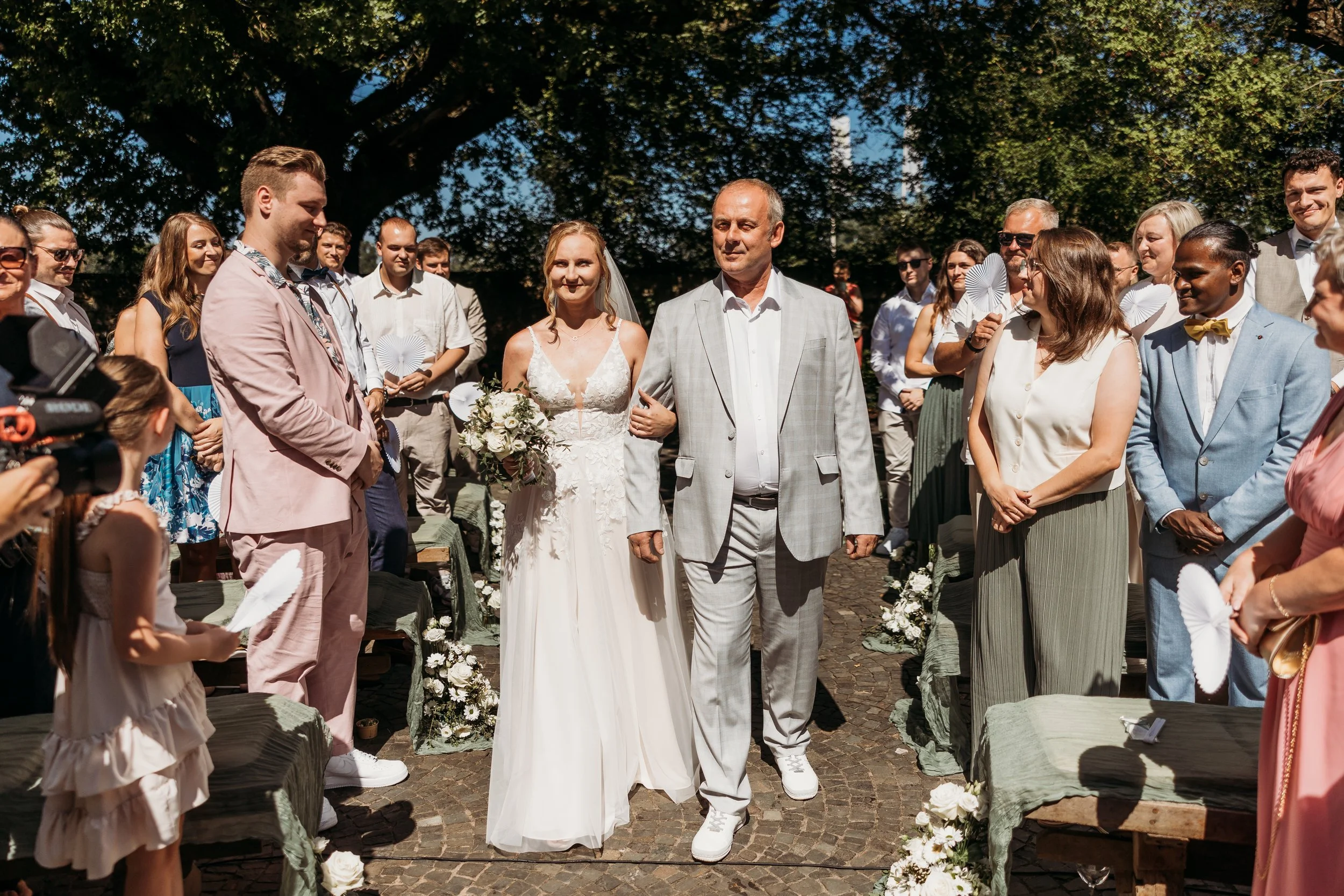Braut und Vater laufen zum Traualtar bei einer Hochzeit im Freien, umgeben von Gästen bei schönem Wetter auf Mathis Wiesenmühle