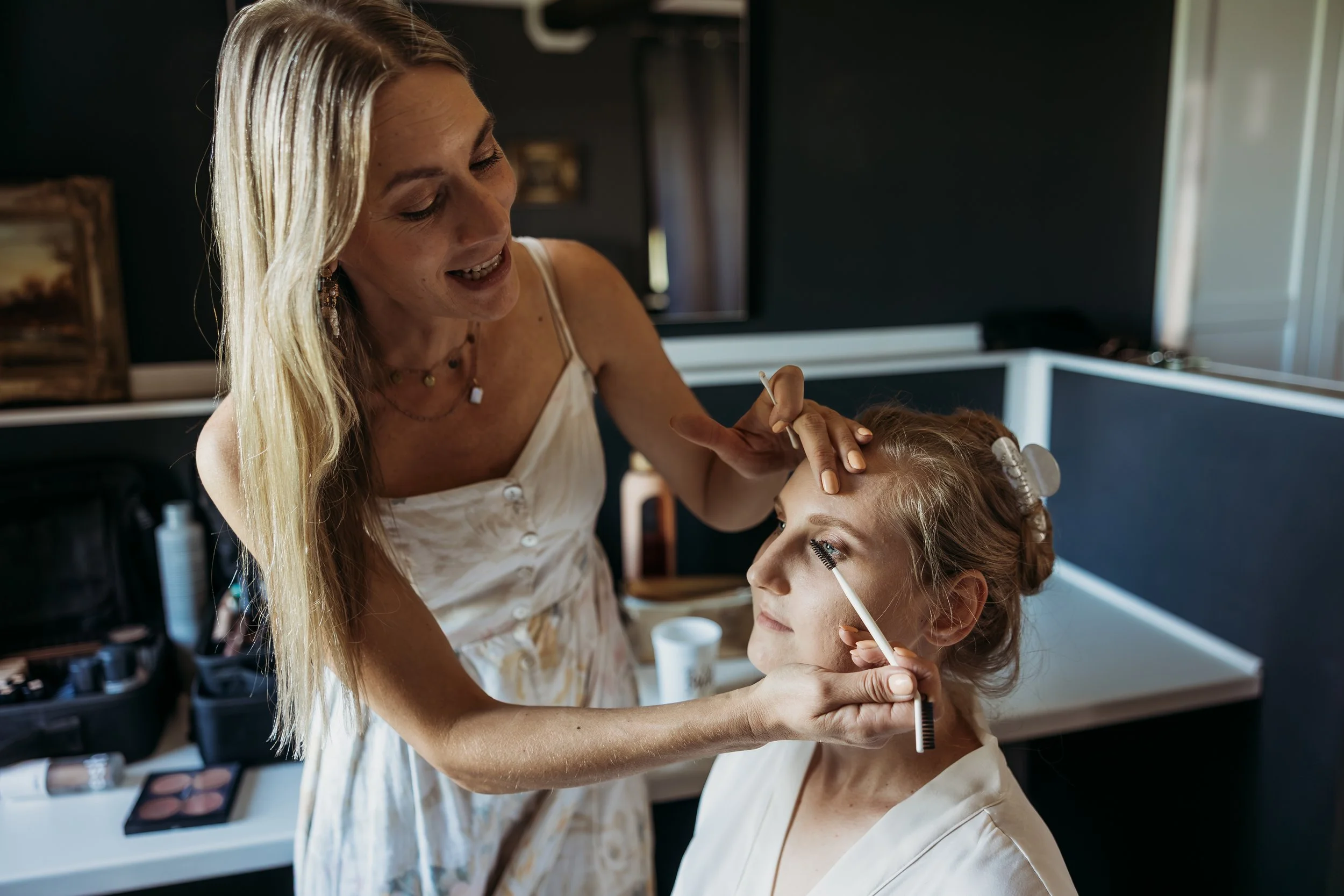 Frau macht Make-up bei einer jungen Frau vor einem Spiegel.