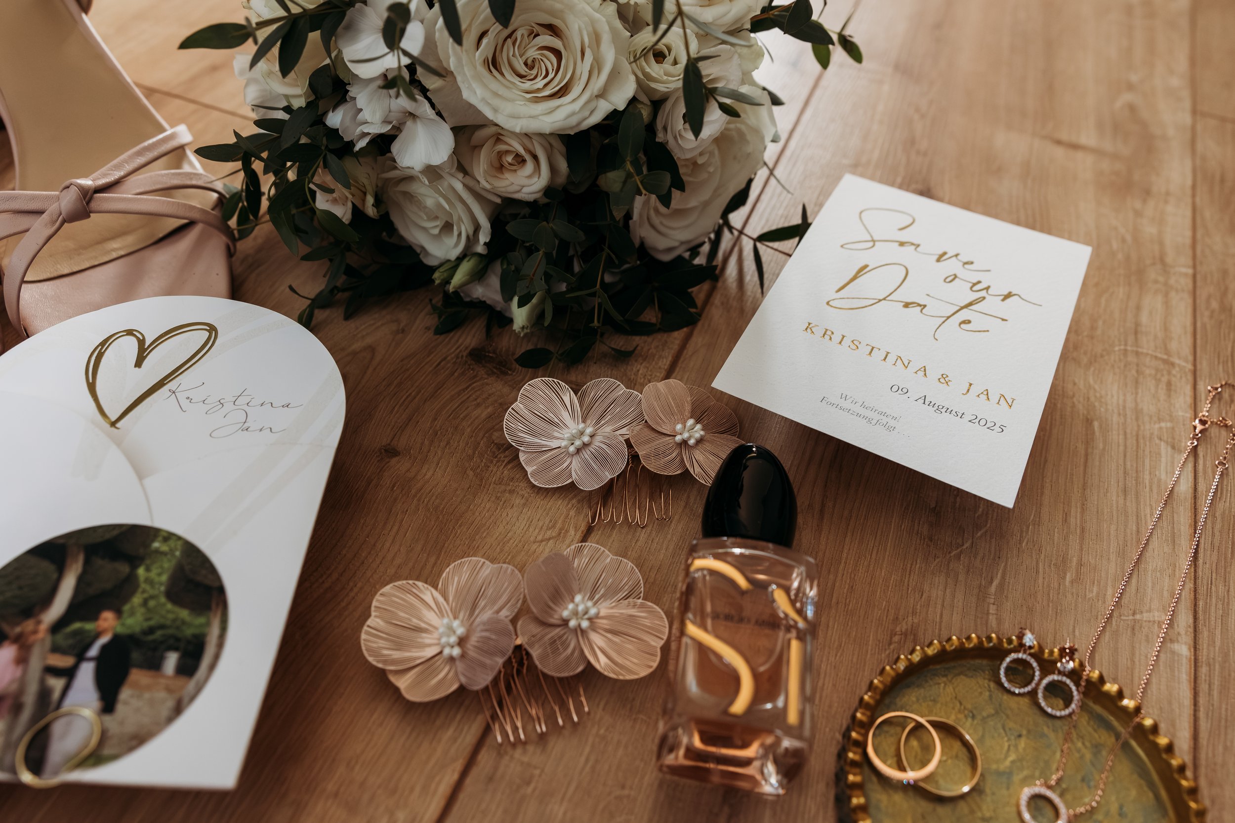 Hochzeitsvorbereitungen mit Braut-Accessoires, Blumen, Save-the-Date-Karten, Parfüm und Schmuck auf einem Holztisch auf Mathis Wiesenmühle