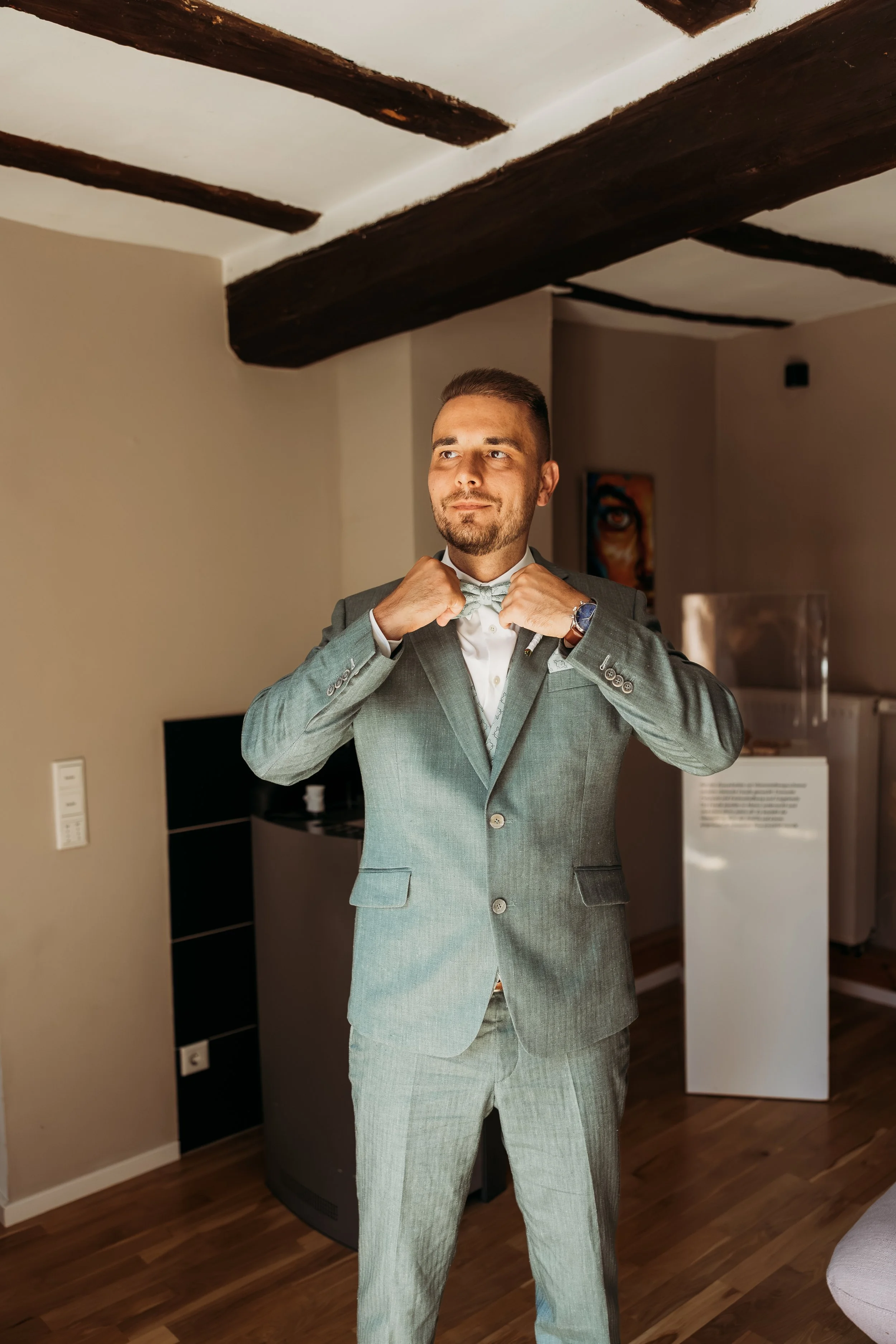Ein Mann in einem grauen Anzug richtet seinen Krawattenknoten, während er sich auf seine Hochzeit  auf Mathis Wiesenmühle vorbereitet